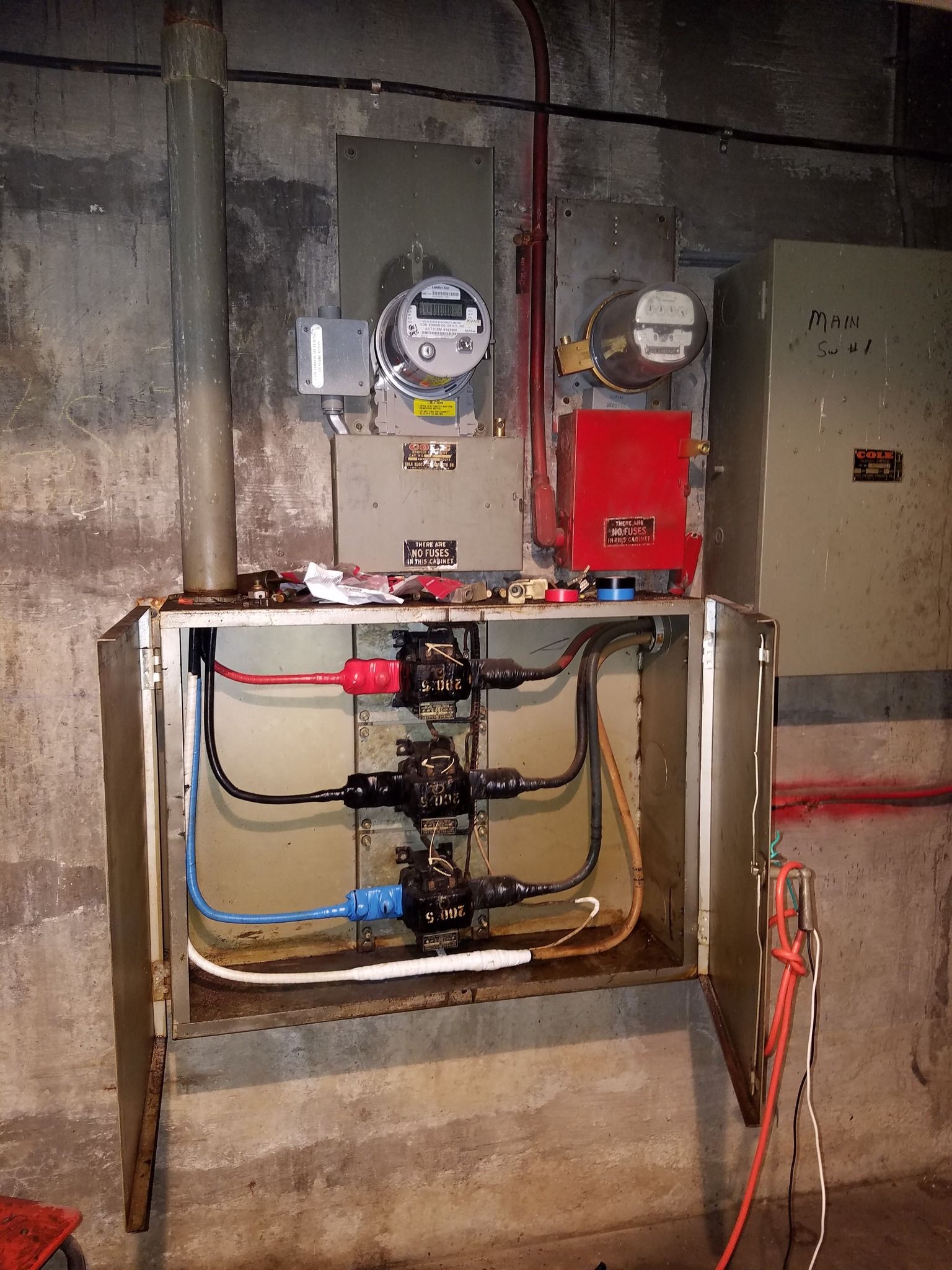 Electrical panel with wiring, meters, and conduits, mounted on a concrete wall.