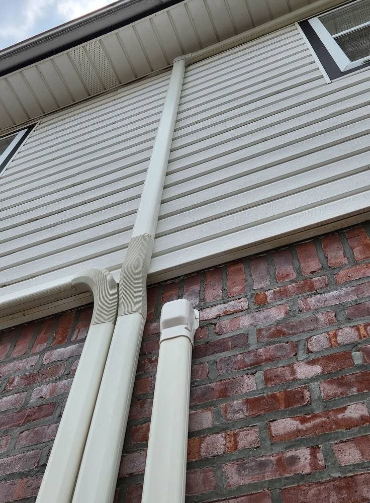 Pipes attached to brick and vinyl siding, likely for an air conditioning system.