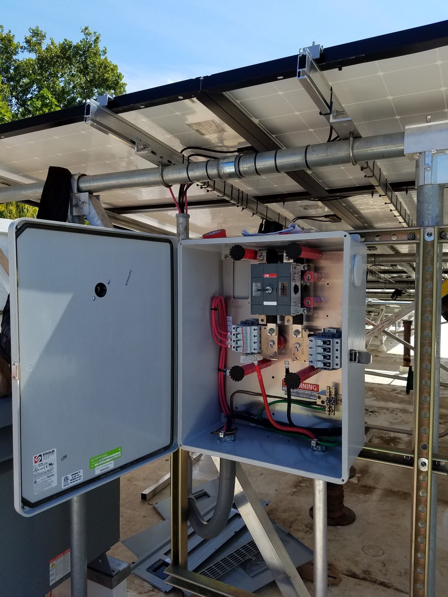 Solar panel electrical box with open door, showing wires and breakers. Outdoor setting.