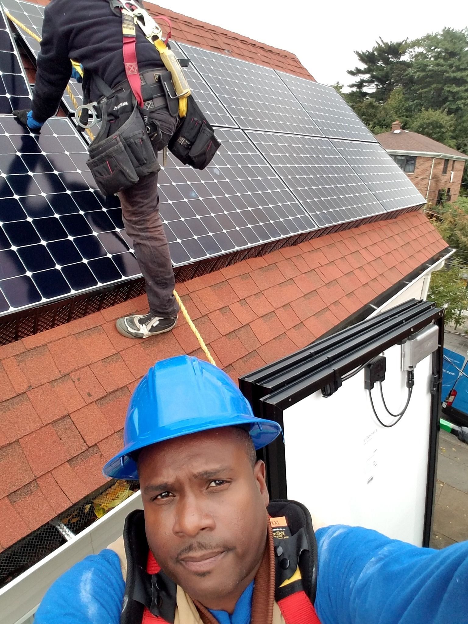 Man in blue helmet on rooftop installing solar panels with another worker.