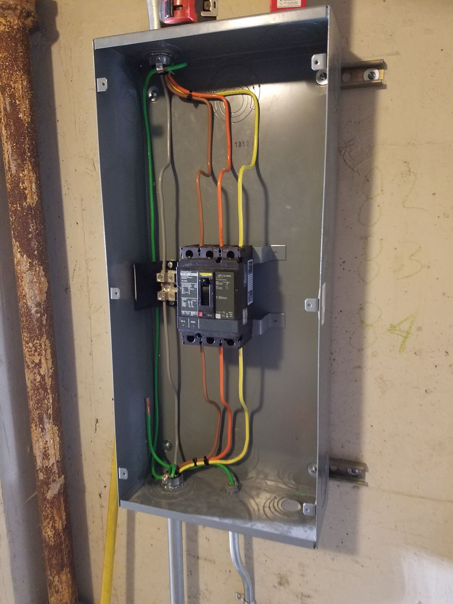Electrical panel with circuit breaker and wires against a concrete wall.