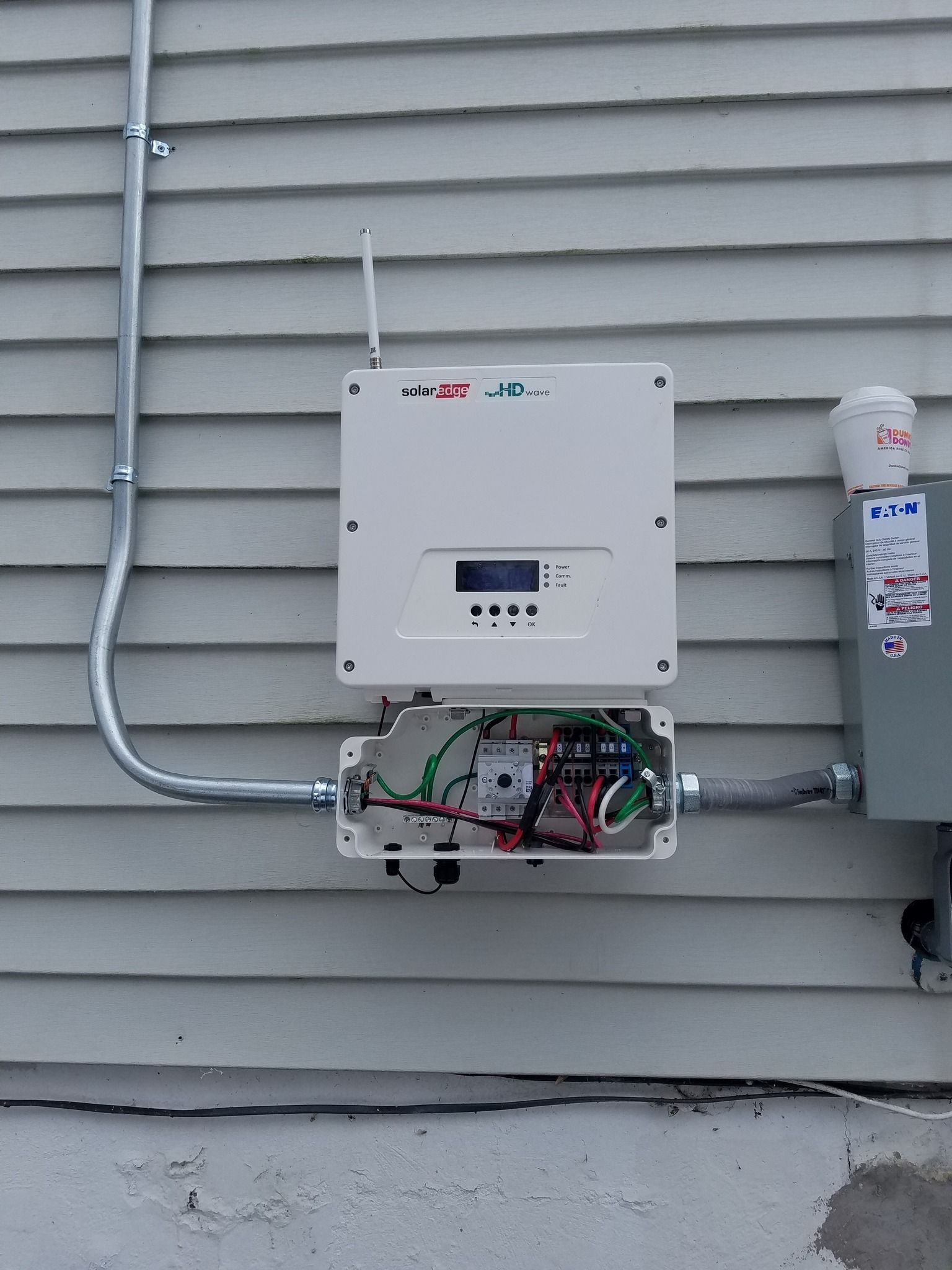 Solar inverter mounted on a white siding wall with wiring.
