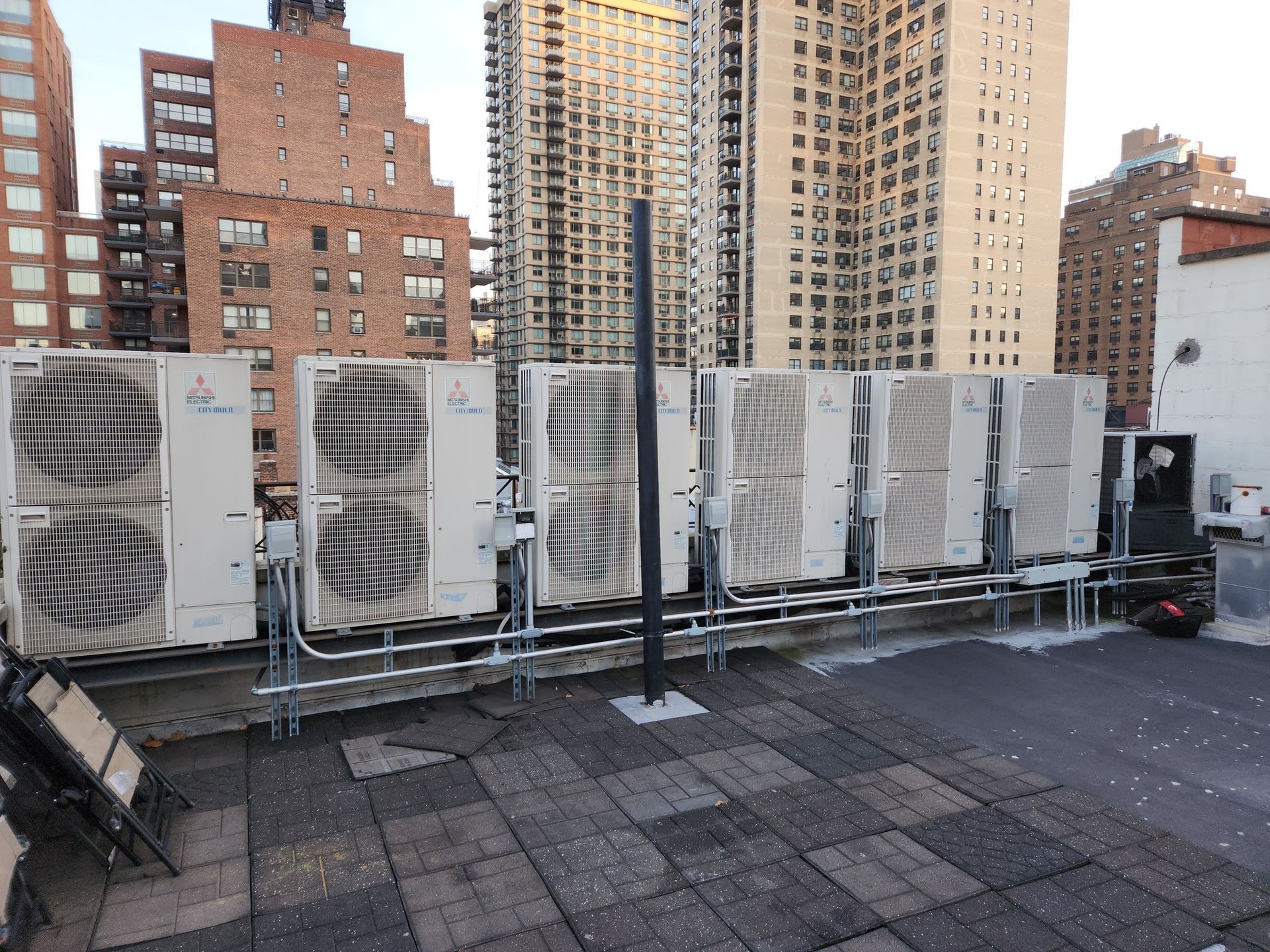 Rooftop with several air conditioning units; brick and glass buildings in the background.