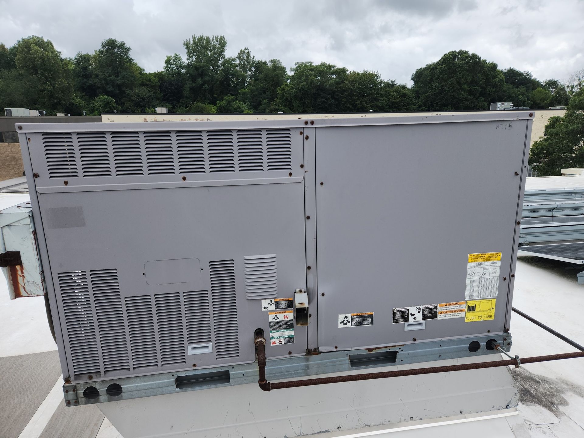Gray HVAC unit on a rooftop with trees in the background.