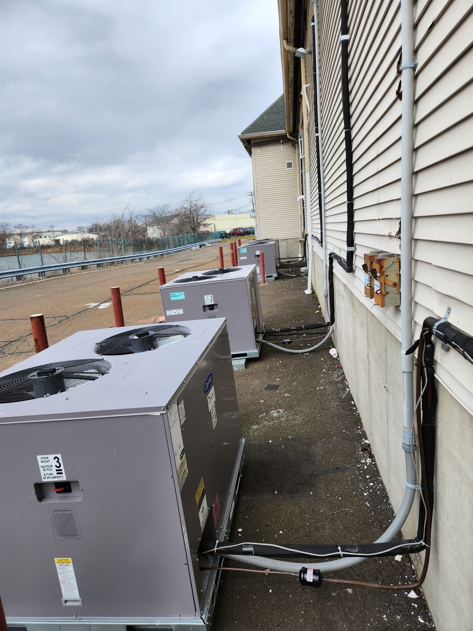 Gray HVAC units lined up on a rooftop next to a building. Cloudy sky and parking lot in background.