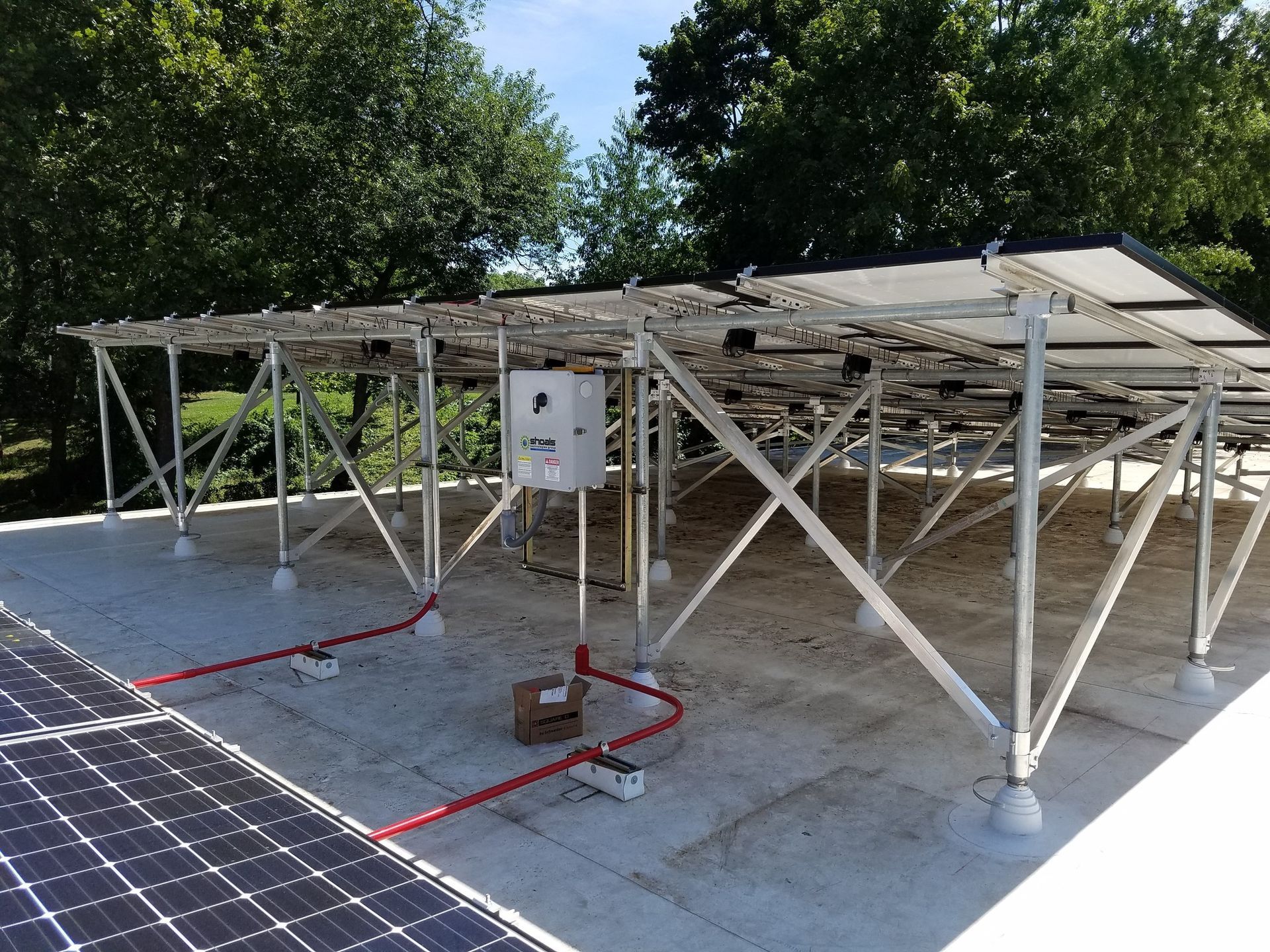 Solar panel array on a white rooftop, supported by a metal frame, with electrical wiring visible.