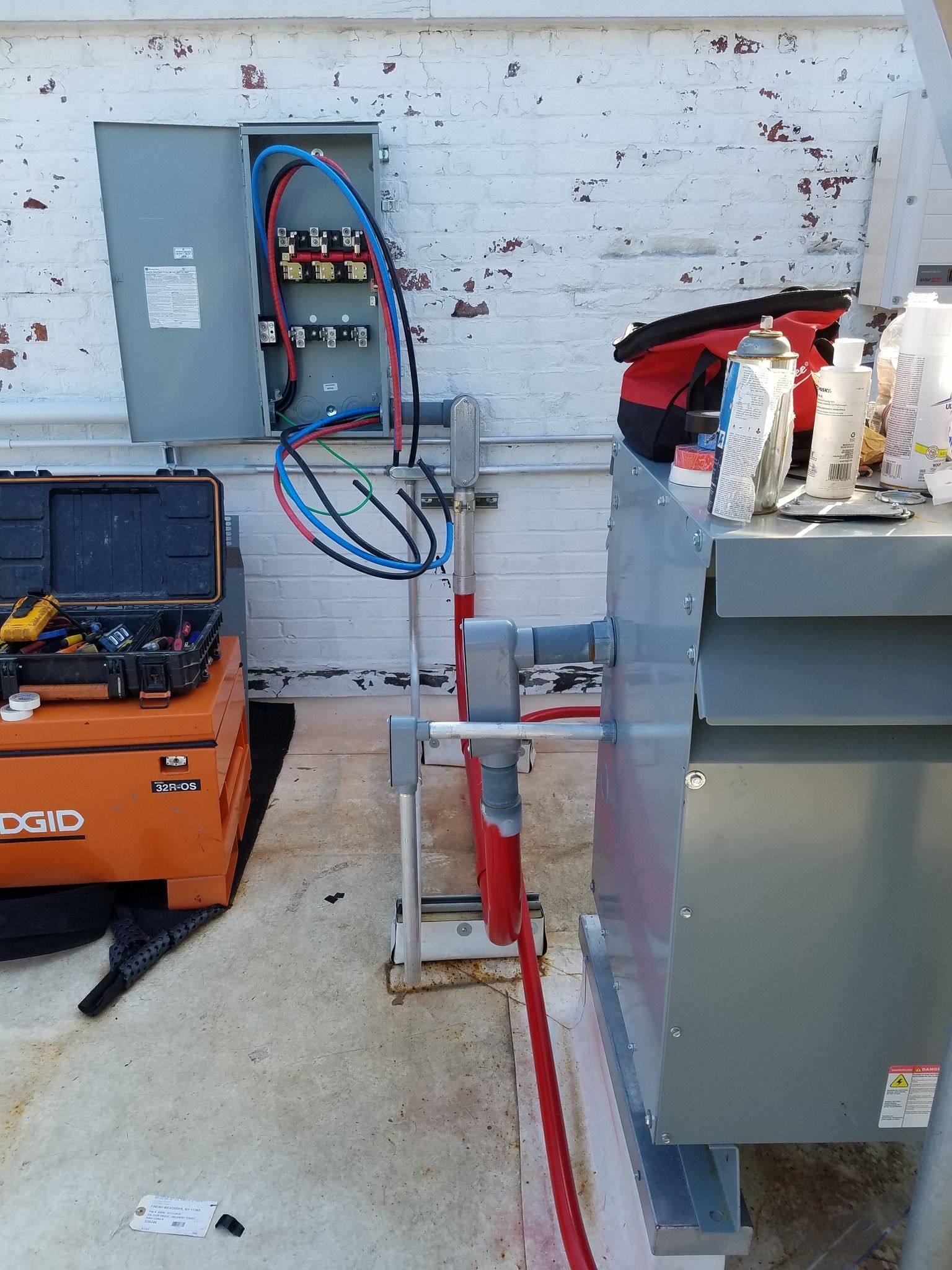 Electrical box and conduit on a brick building's exterior, with tools and a generator nearby.