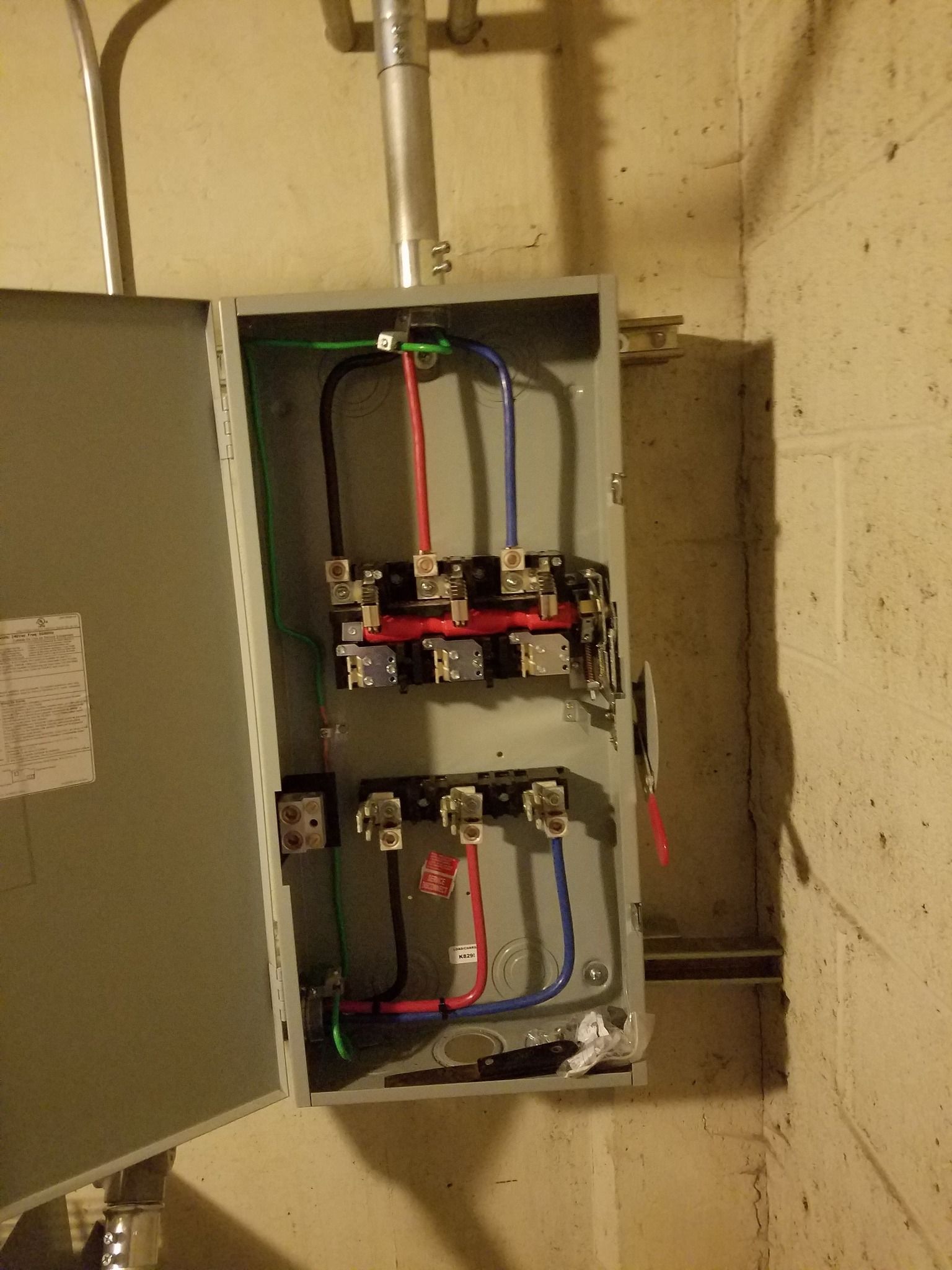 Open electrical panel with wires and circuit breakers mounted on a concrete wall.