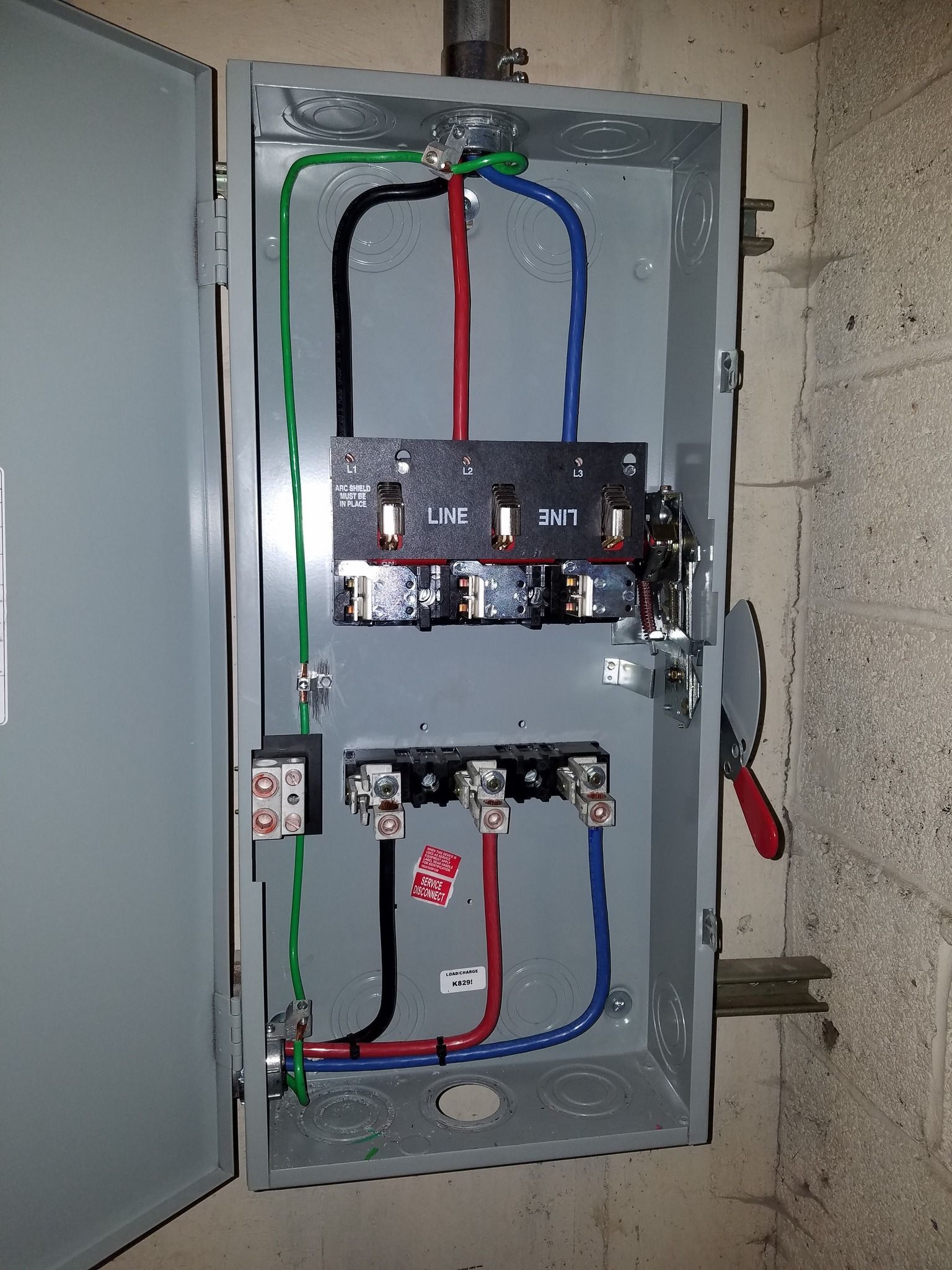 Open electrical panel with black, red, and blue wires, and green grounding wire.