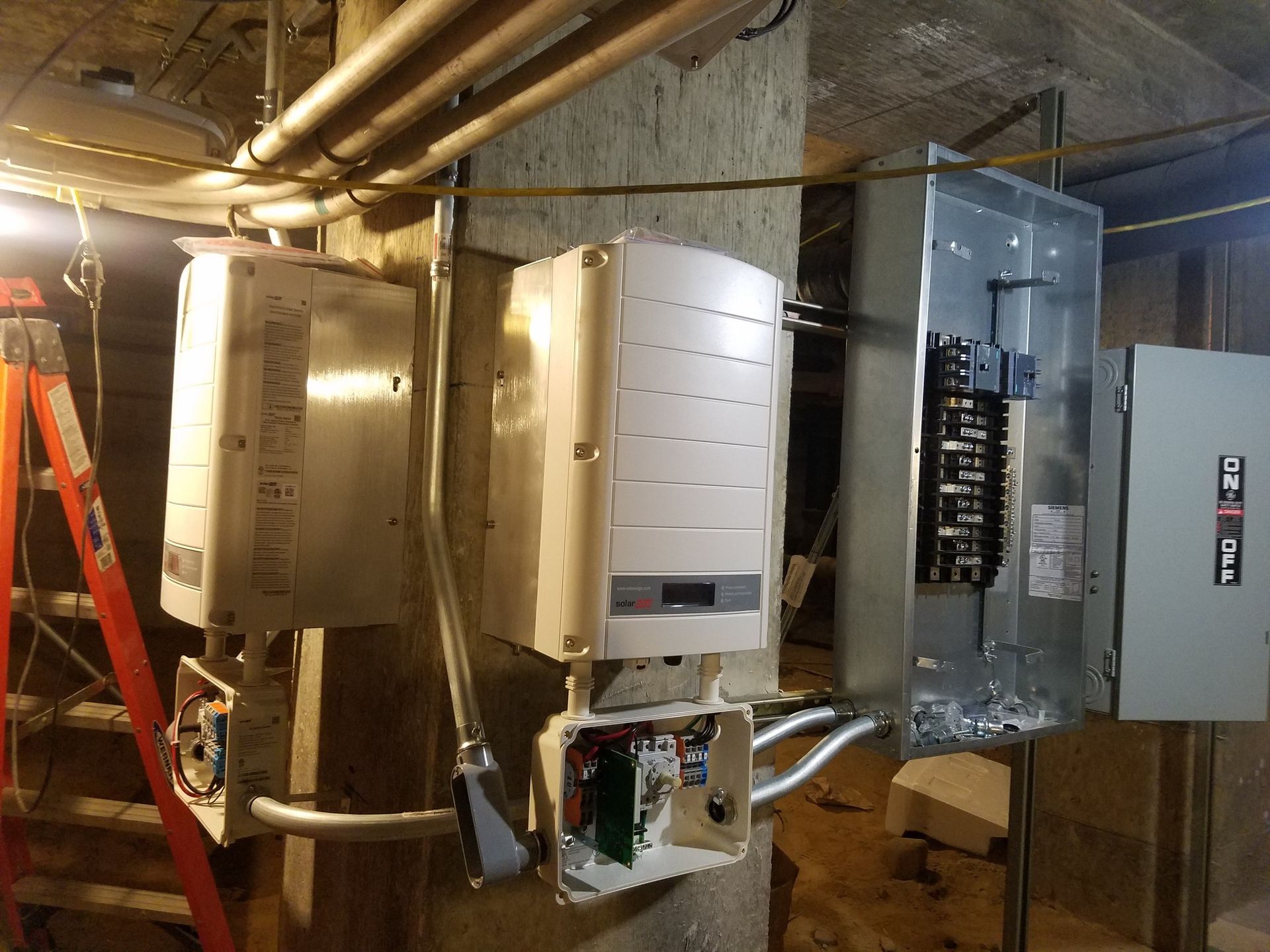 Electrical components mounted on a concrete pillar; includes breaker box, inverters, and conduit.