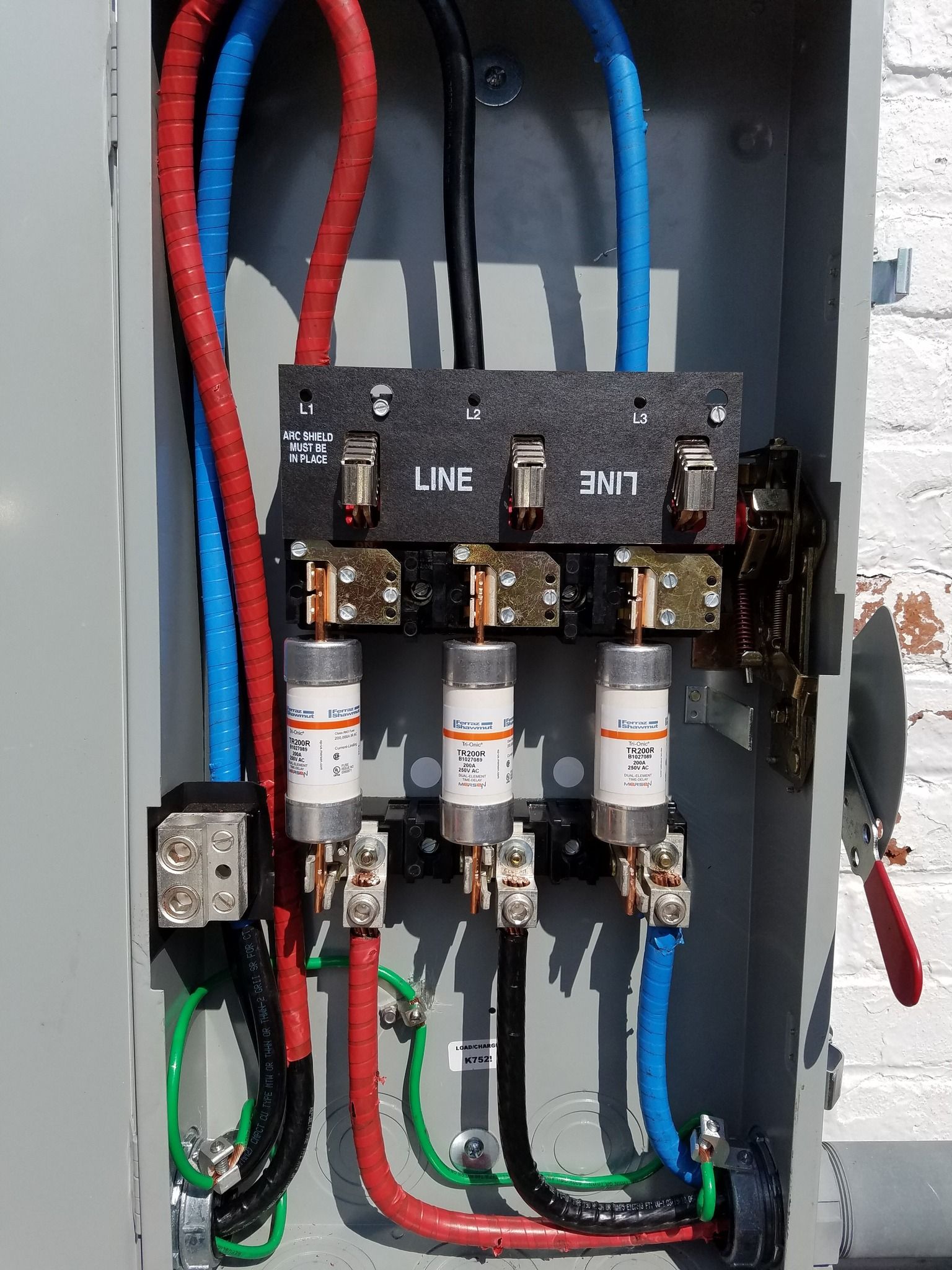 Electrical panel with three fuses, red, black, and blue wires, and green grounding wires.