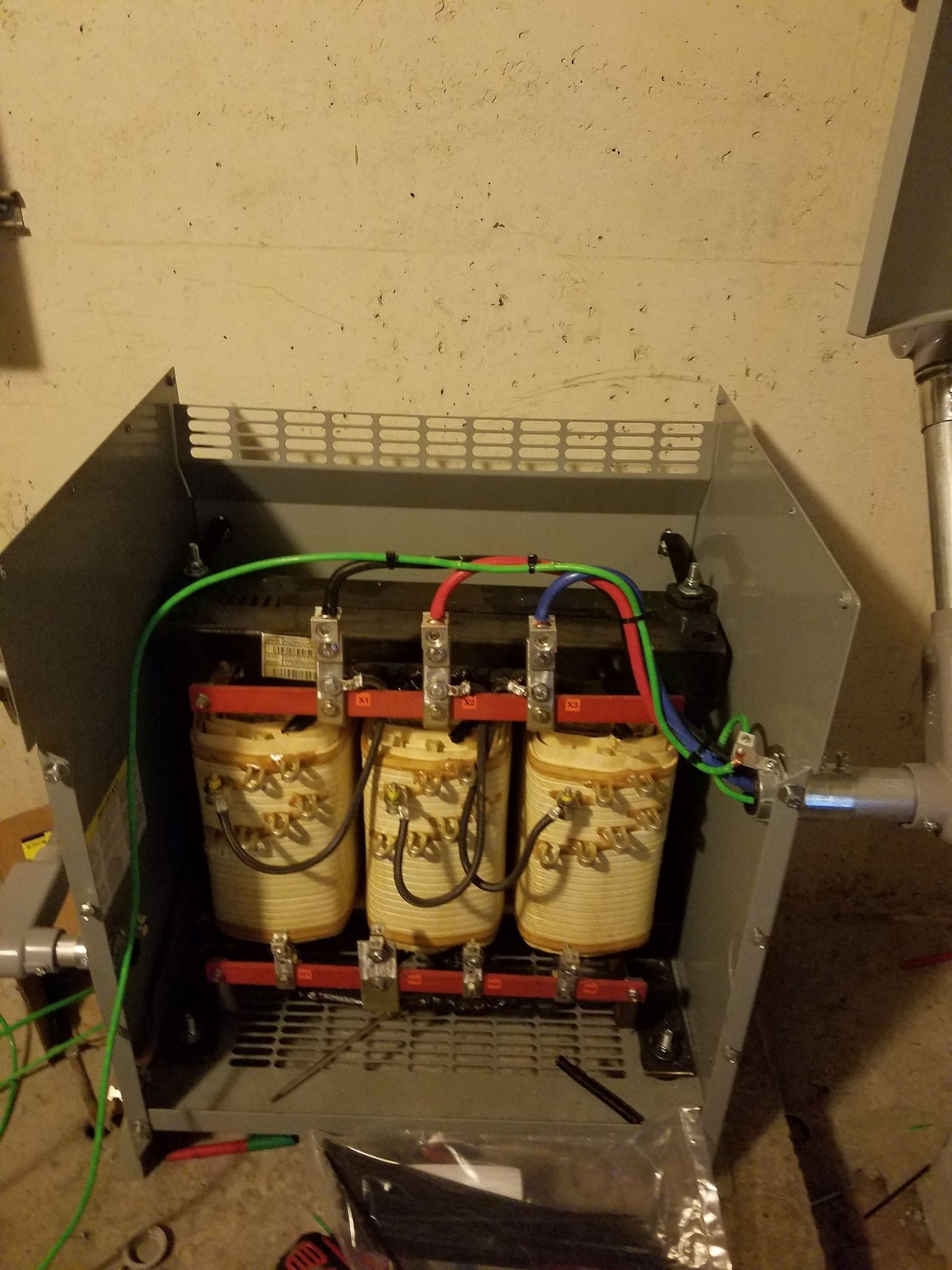 Three-phase transformer inside a metal enclosure. Green, red, and blue wires connect to terminals.