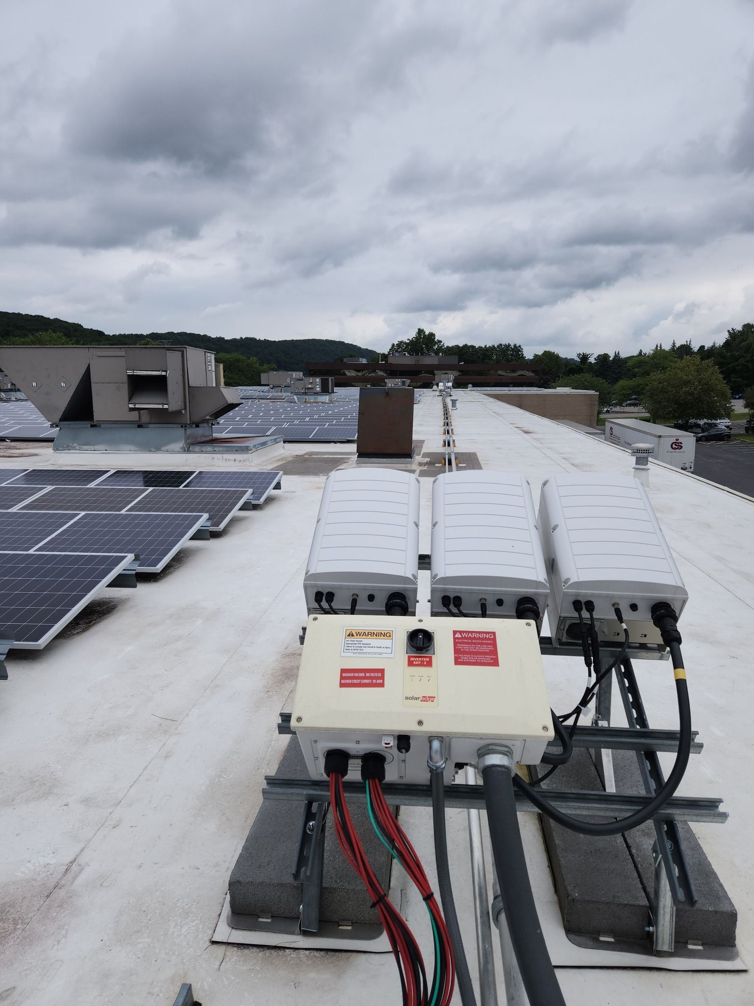 Solar panel installation on a flat roof with inverters and wiring visible. Overcast sky in background.
