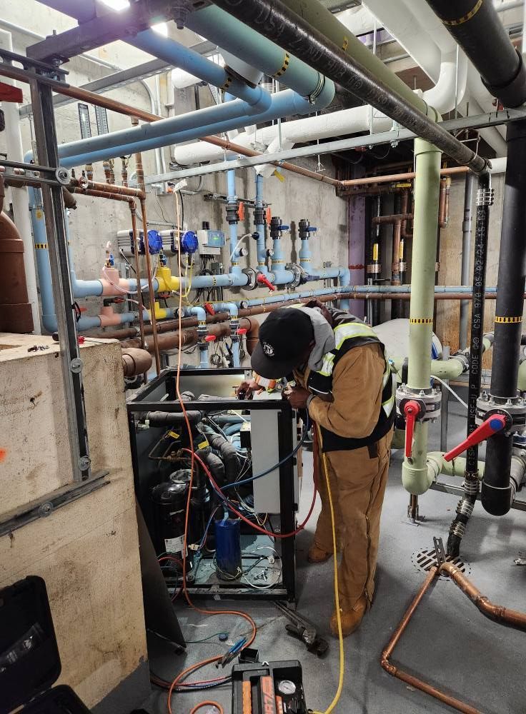 Mechanic working on machinery in a mechanical room, surrounded by pipes.