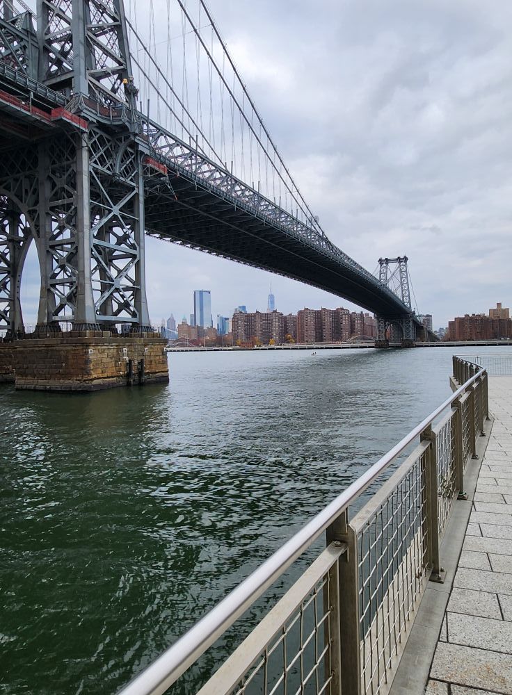 Williamsburg Bridge over the East River with city skyline in the background, cloudy day.