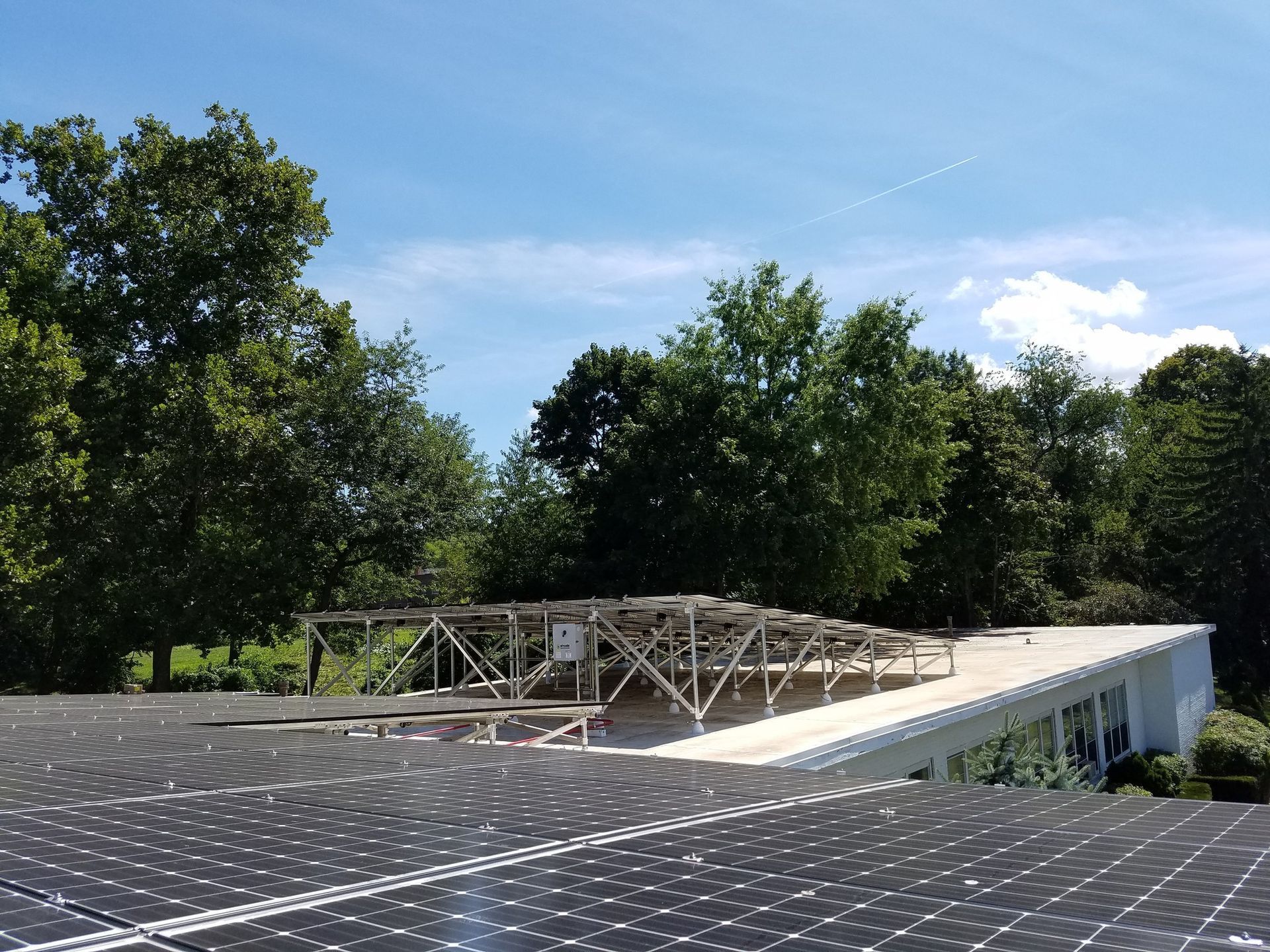 Solar panels on a roof with a wooden structure being built, trees and blue sky.