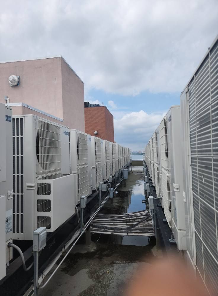 Rooftop with rows of air conditioning units, against a cloudy sky.