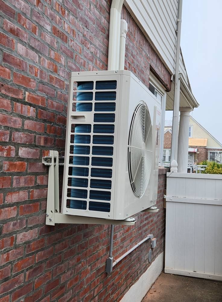 White air conditioning unit mounted on a red brick wall, next to a white house.