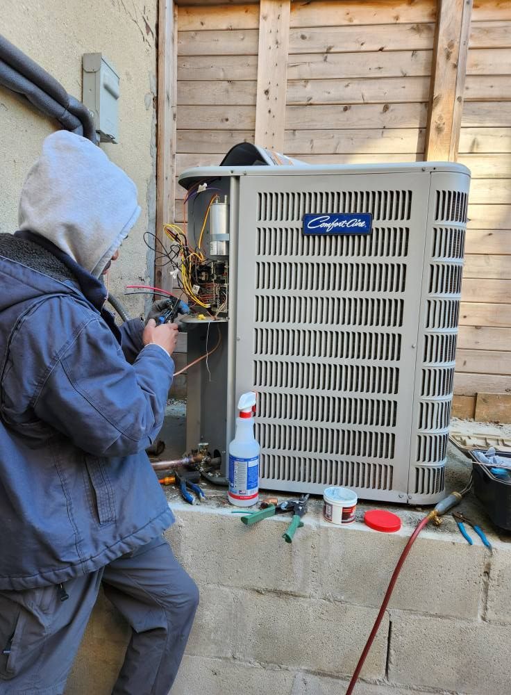 Person in a hooded jacket repairing an air conditioning unit outdoors.