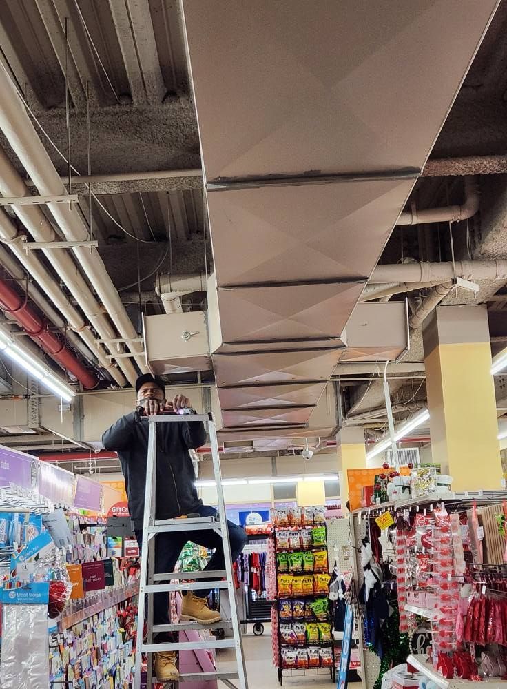 Person on a ladder working on overhead ventilation ducts in a store.