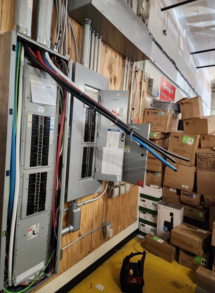 Electrical panel with exposed wires on a wood wall next to stacked boxes.