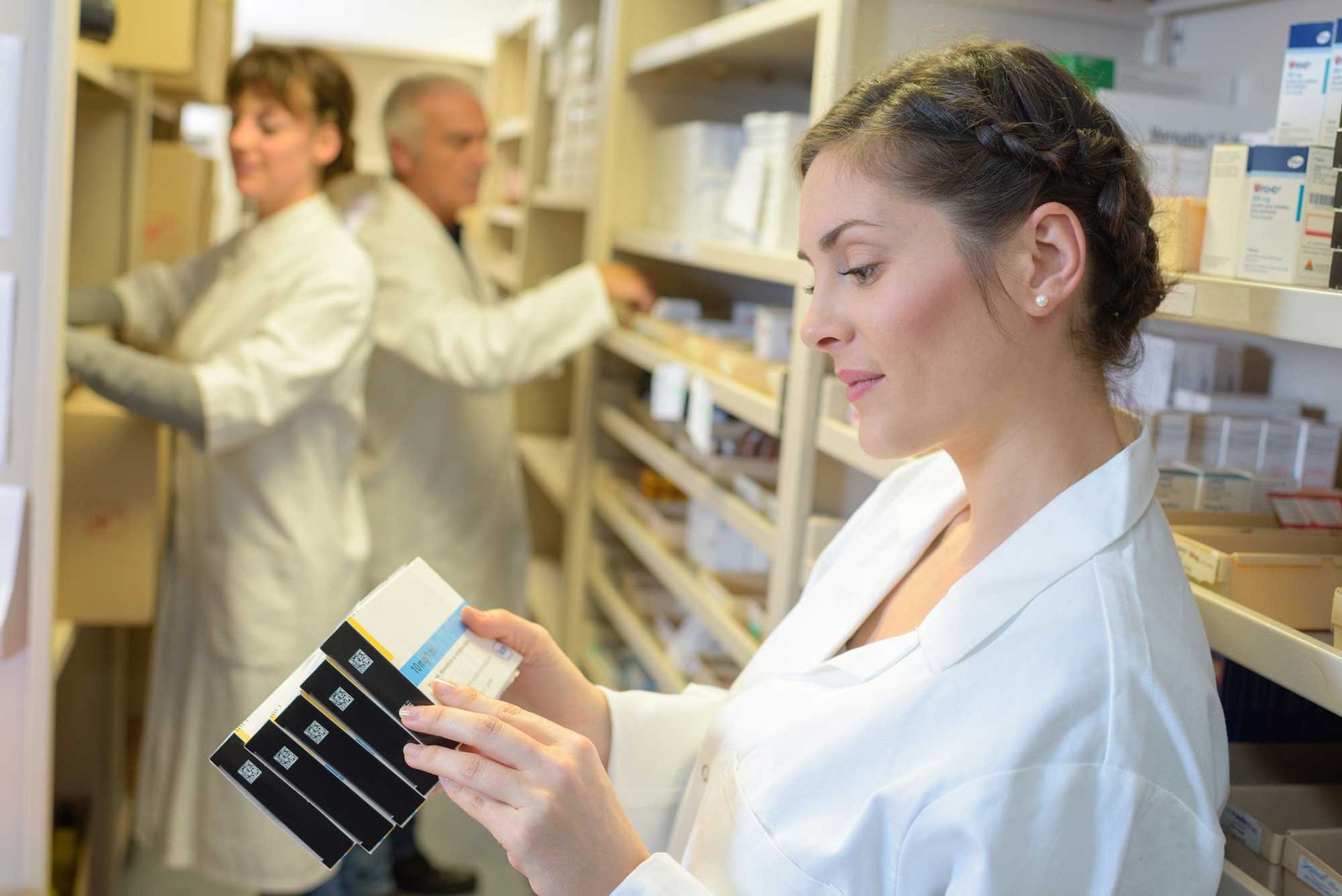 A lab worker checking medications in a pharmaceutical company. Two others are in the background.
