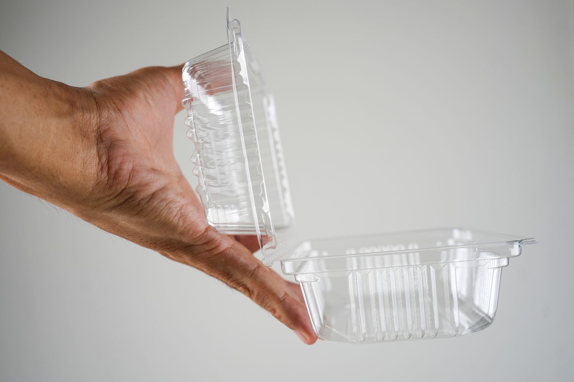Cropped hand holding a plastic food container.