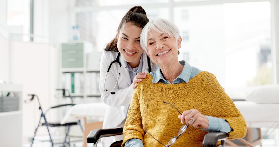 Doctor smiles with patient in wheelchair; medical office setting.