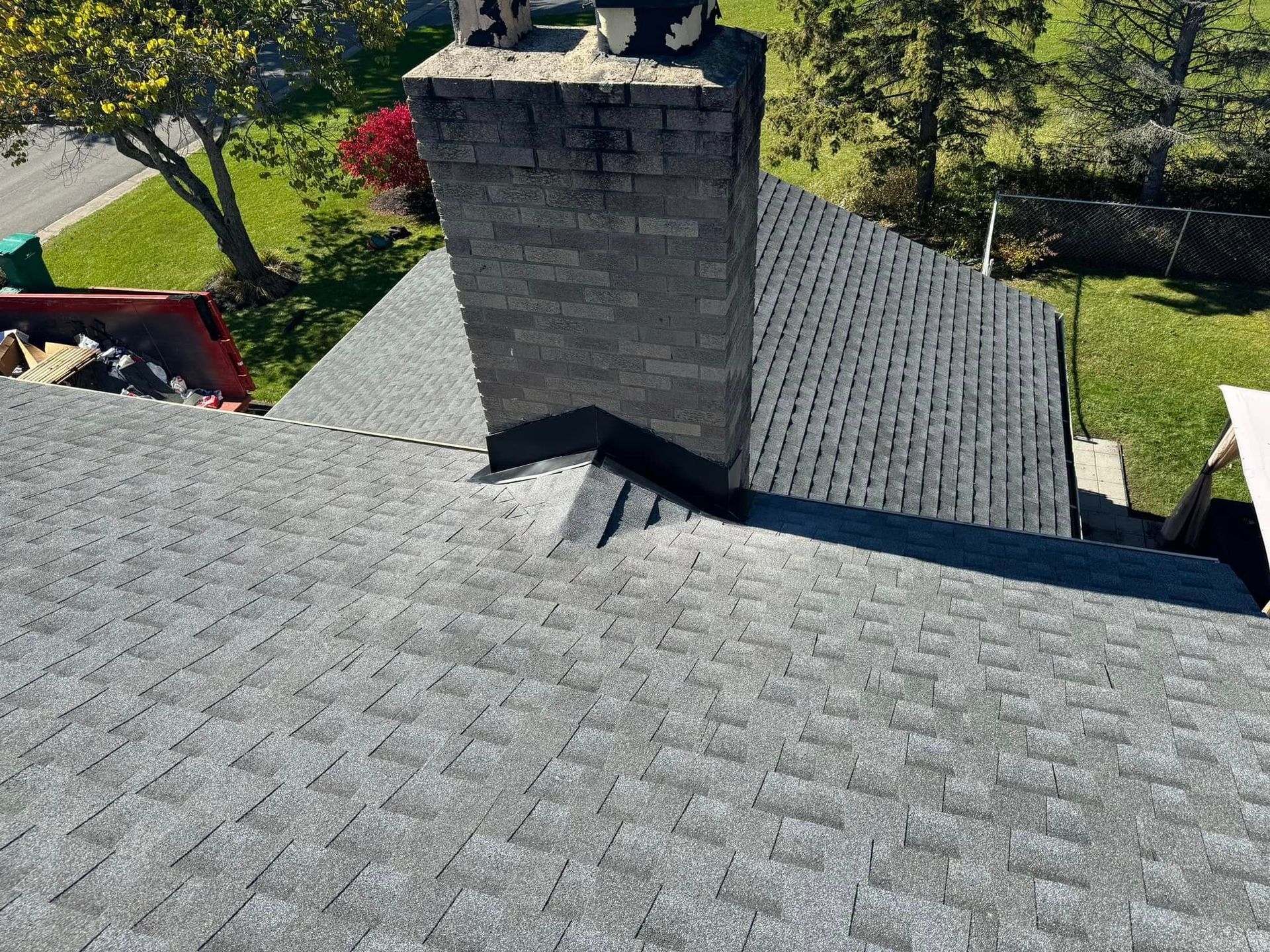 Gray shingle roof with a brick chimney; daytime with green lawn and trees.
