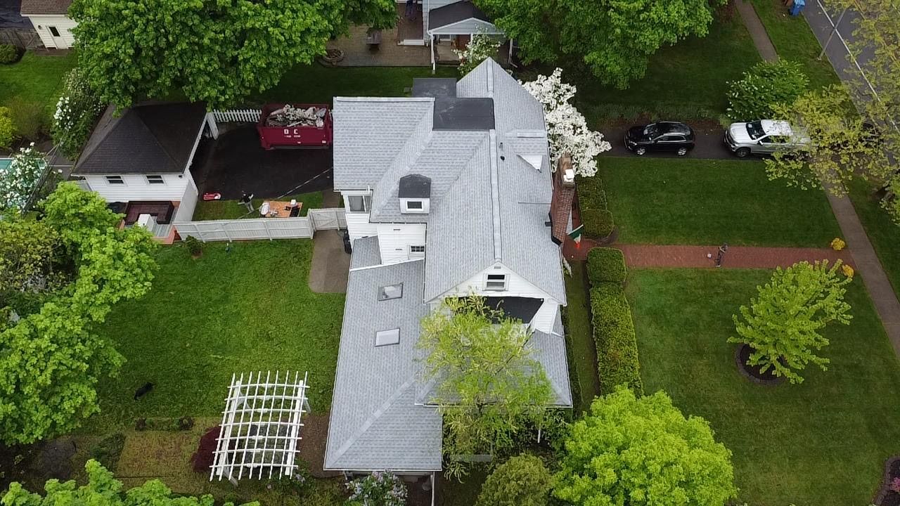 Overhead view of a house with gray roof, green lawn, and two cars parked on the street.