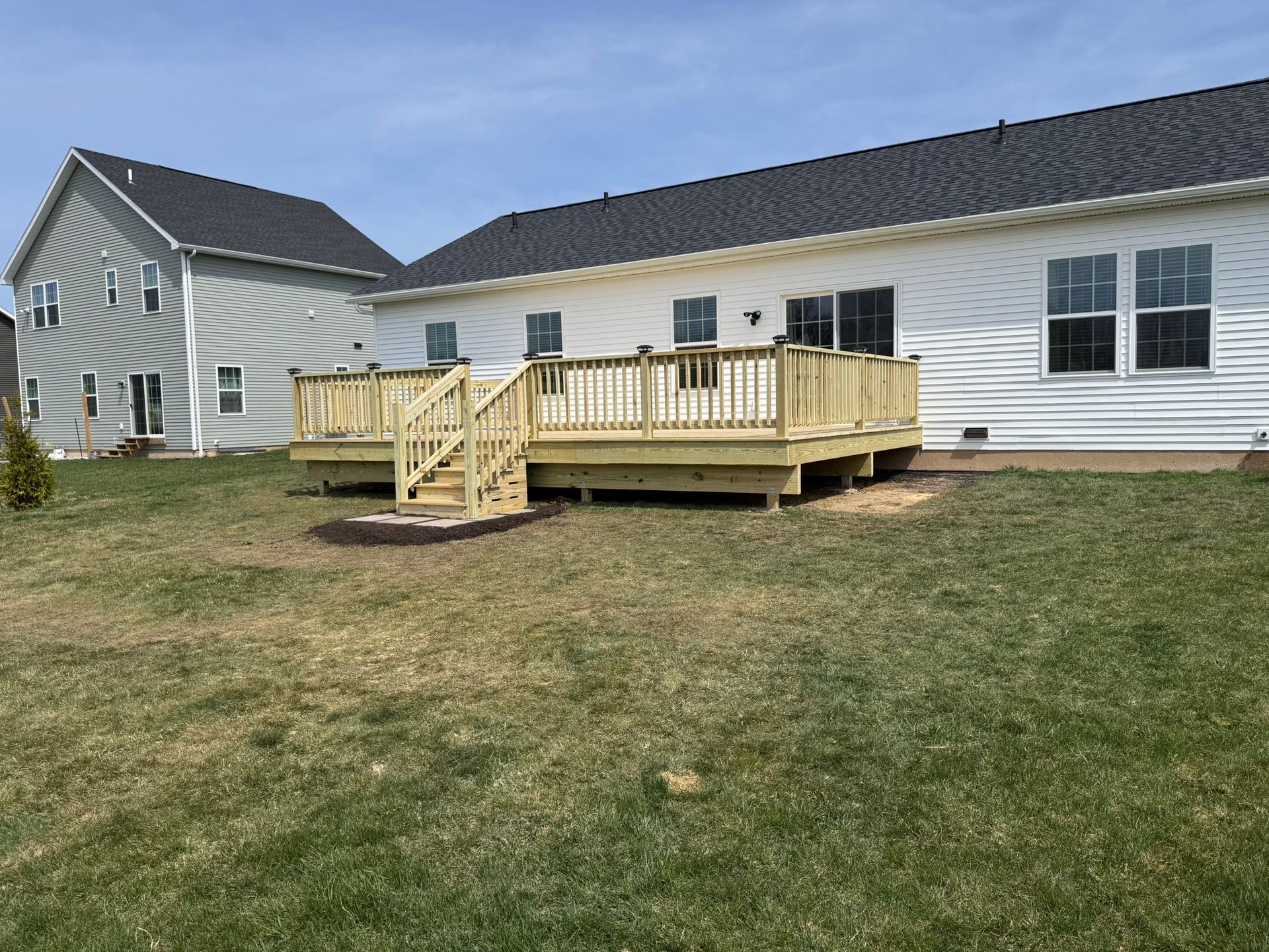 Wooden deck attached to a white house, with steps leading down to a grassy yard.
