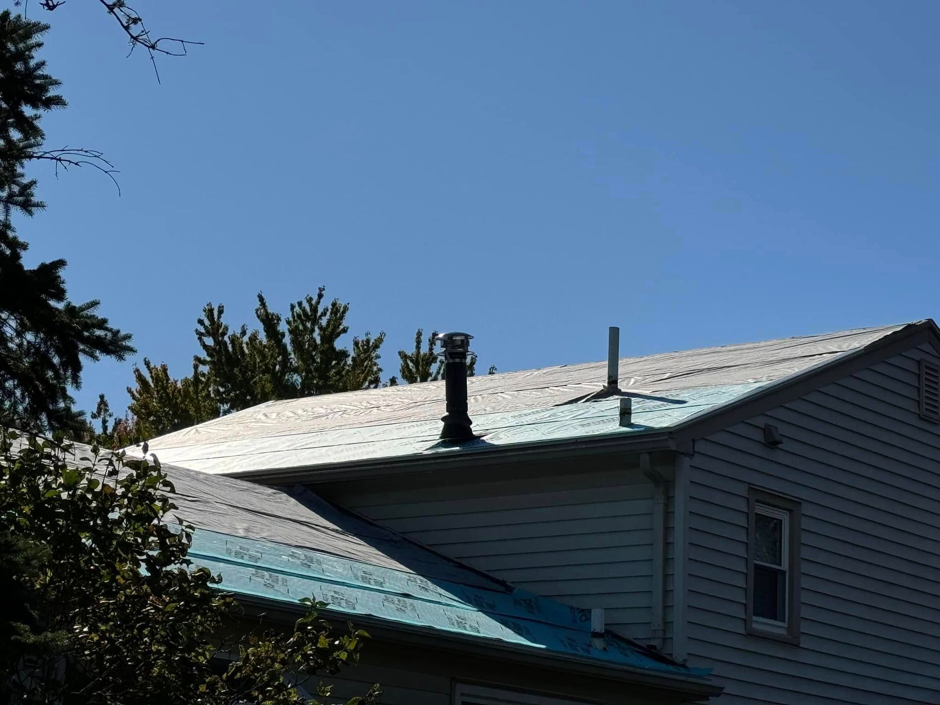 Blue and silver metal roof with chimneys on a house against a clear blue sky.
