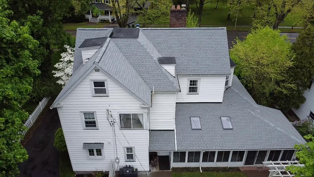 White house with gray roof, two stories, surrounded by trees.