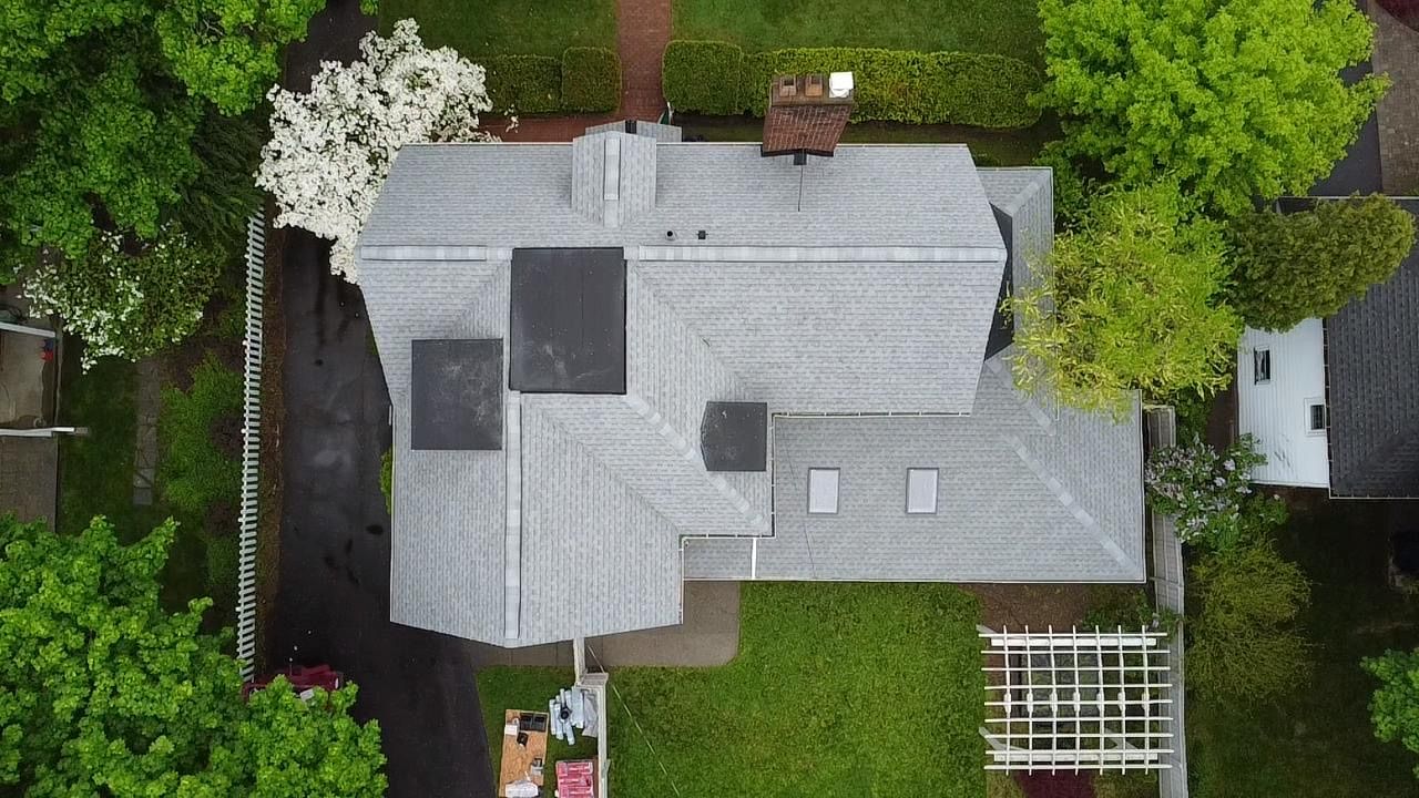 Overhead view of a house with a grey roof surrounded by green trees and a lawn.