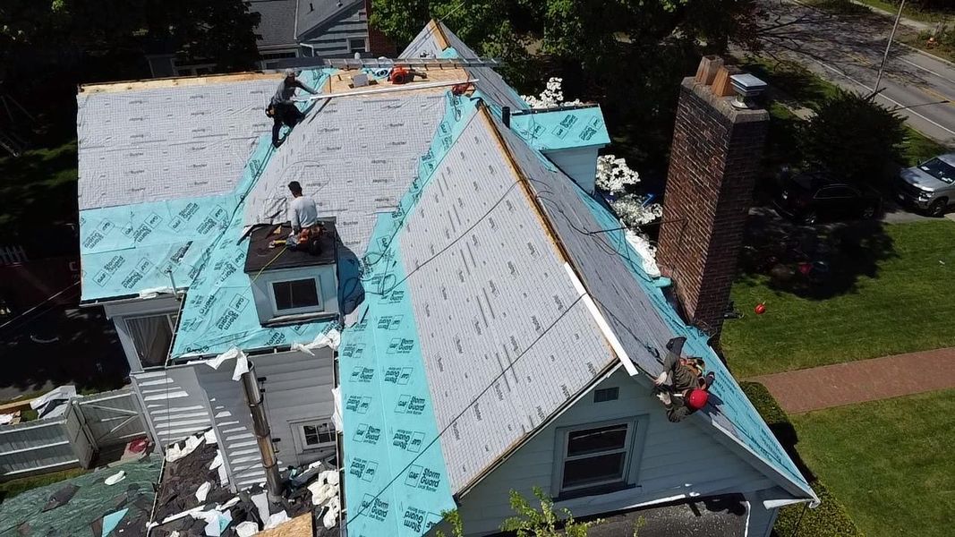 Roofers replacing shingles on a house, with blue underlayment visible.