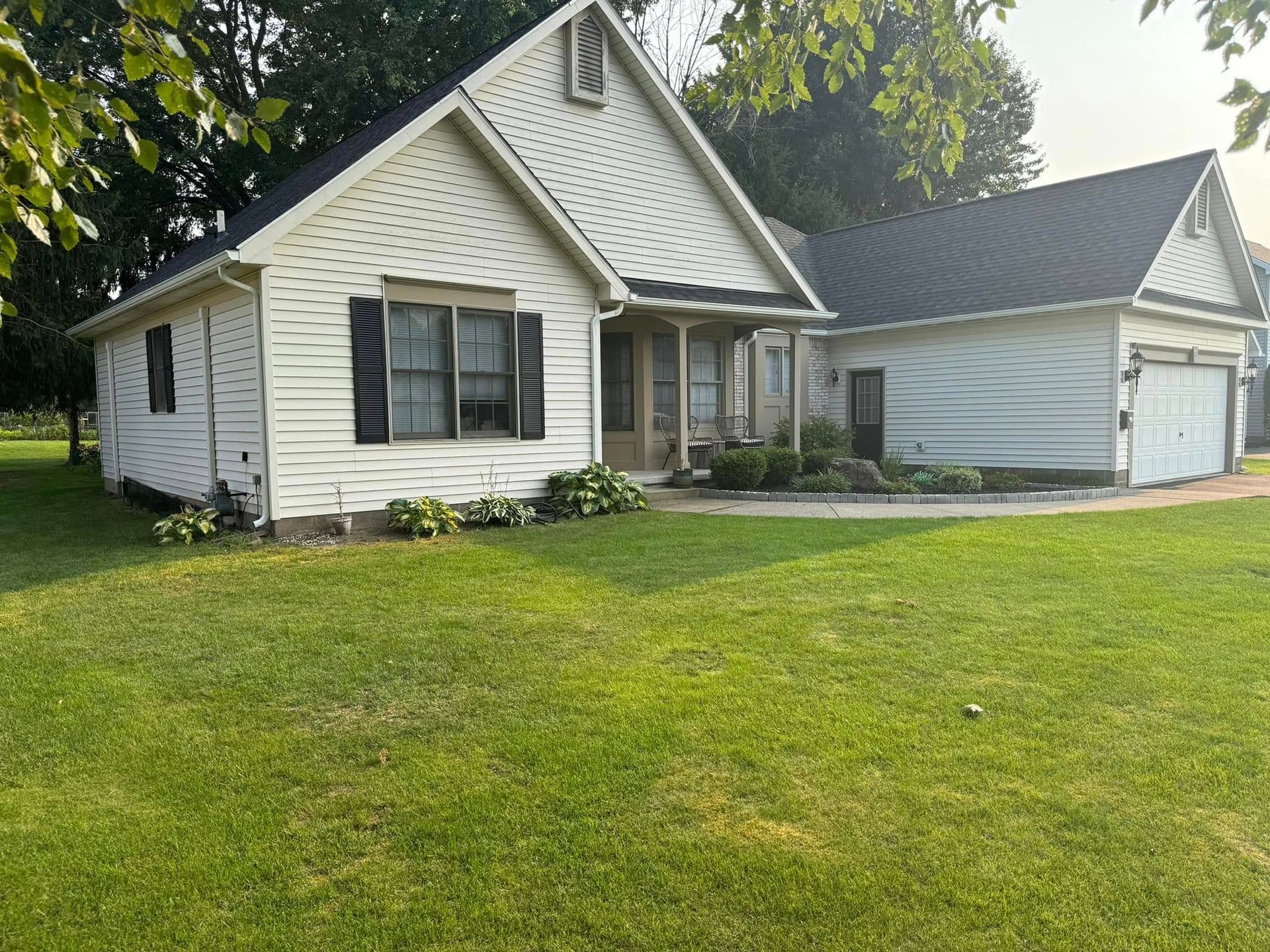 White house with black shutters and a detached garage, set in a grassy yard.