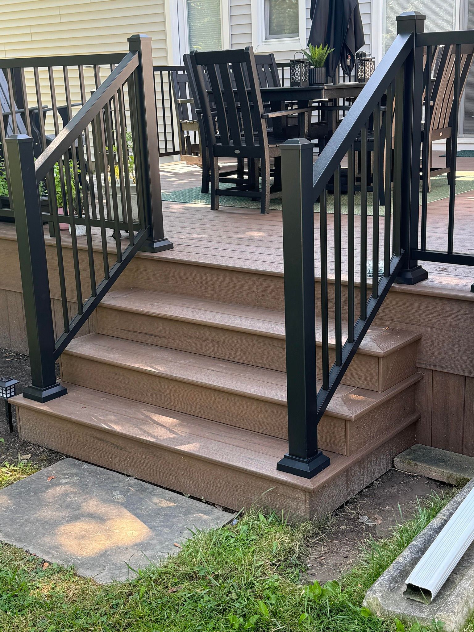 Deck stairs with black railing. Brown steps and deck. Outdoor setting with furniture.