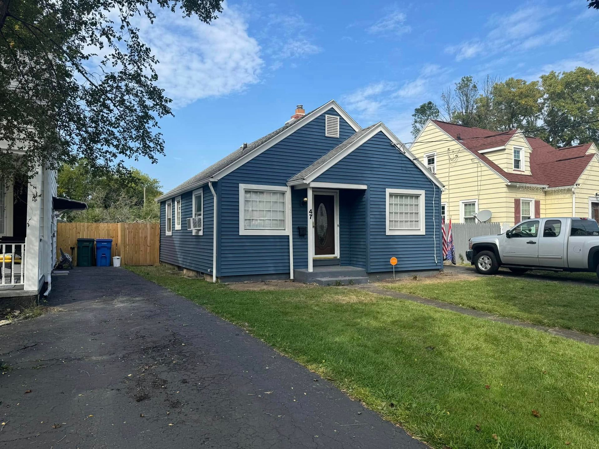 Blue house with green lawn and black driveway. A white truck sits to the right.