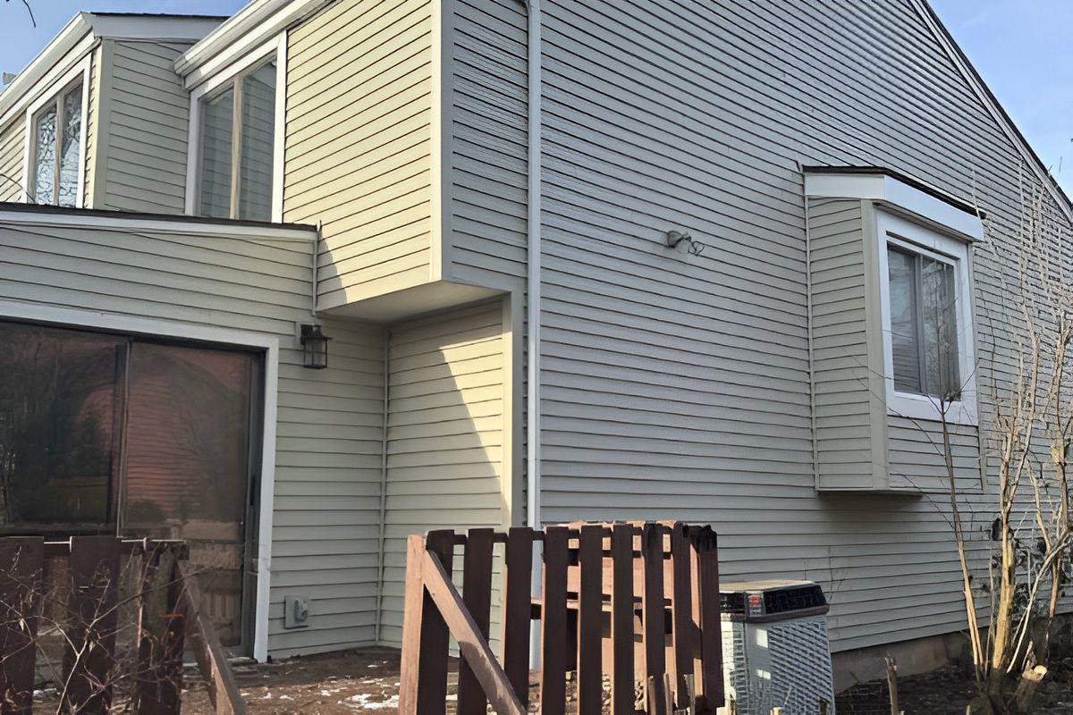 Beige siding covers a two-story house with a small deck, windows, and a bay window.