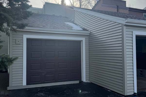 Tan siding with a brown garage door framed in white; snow on roof edge.