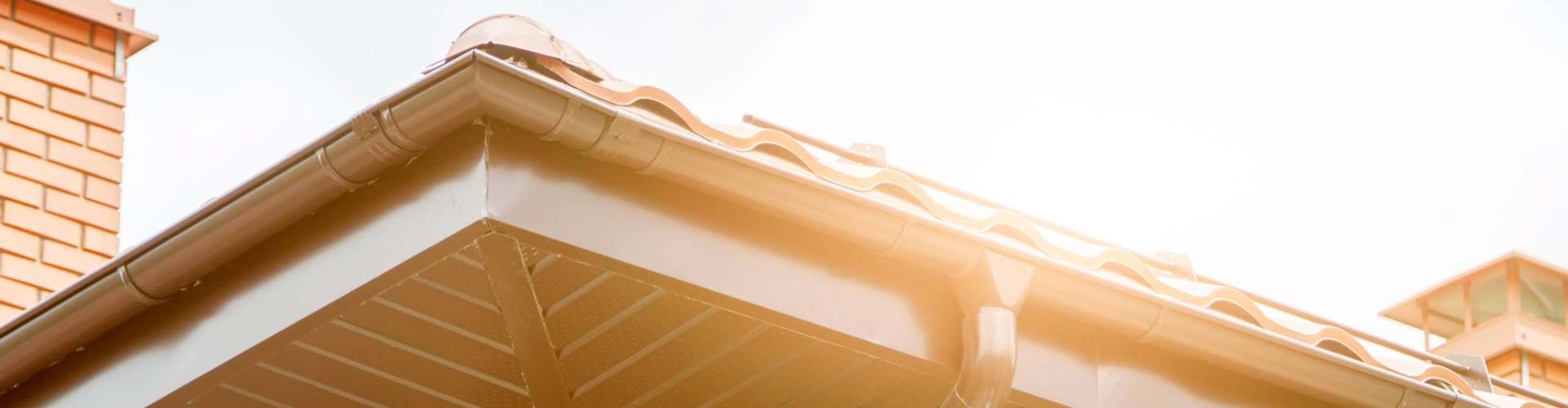 Brown roofline with brick chimney and a sunny sky.