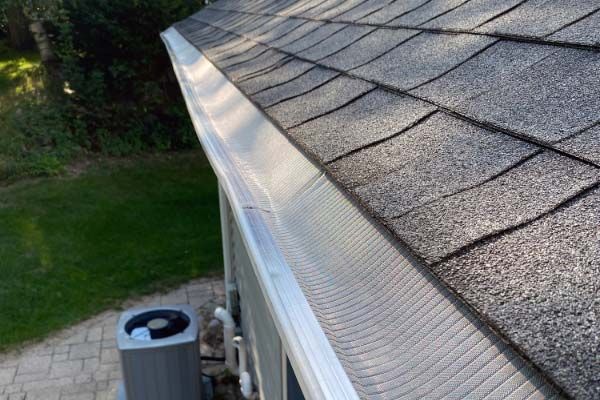 Gutter guard on a roof with gray shingles, next to the house and a grassy yard.