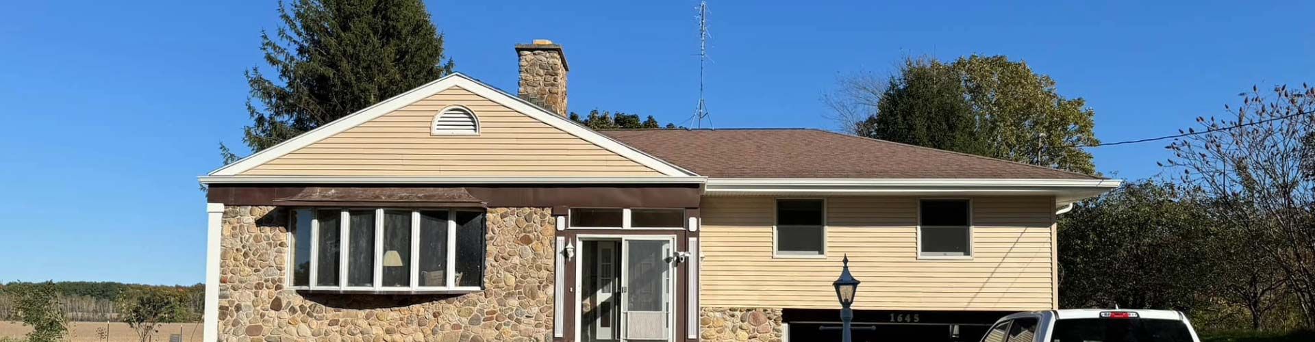A two-story house with a stone facade, brown roof, and clear blue sky.