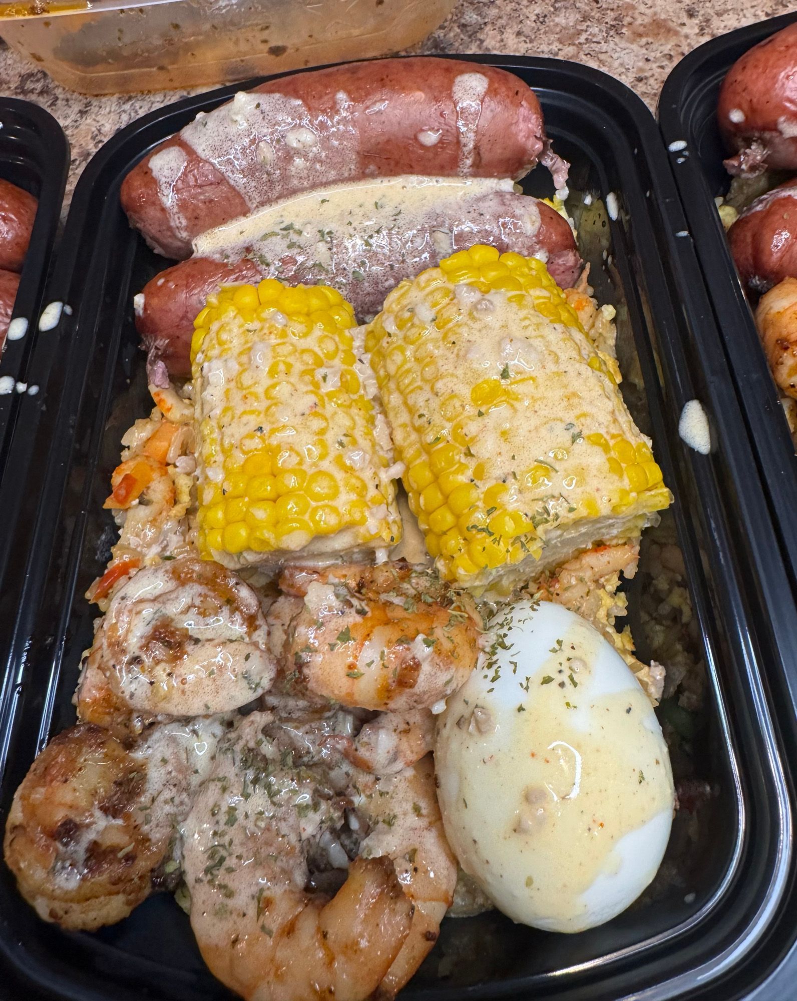 A tray of food with corn on the cob , shrimp , potatoes and eggs.