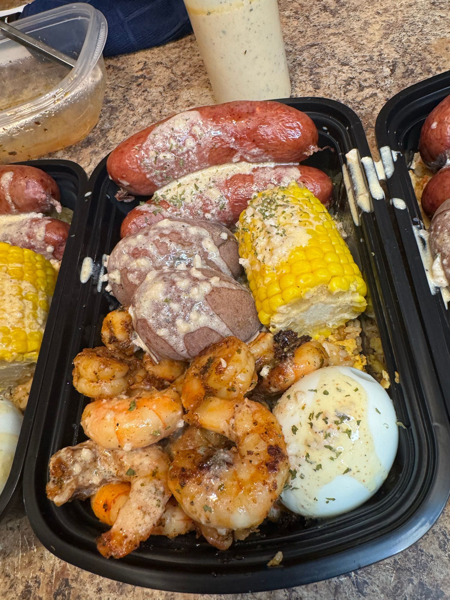 A plastic container filled with shrimp , corn on the cob , sausage , potatoes and eggs.