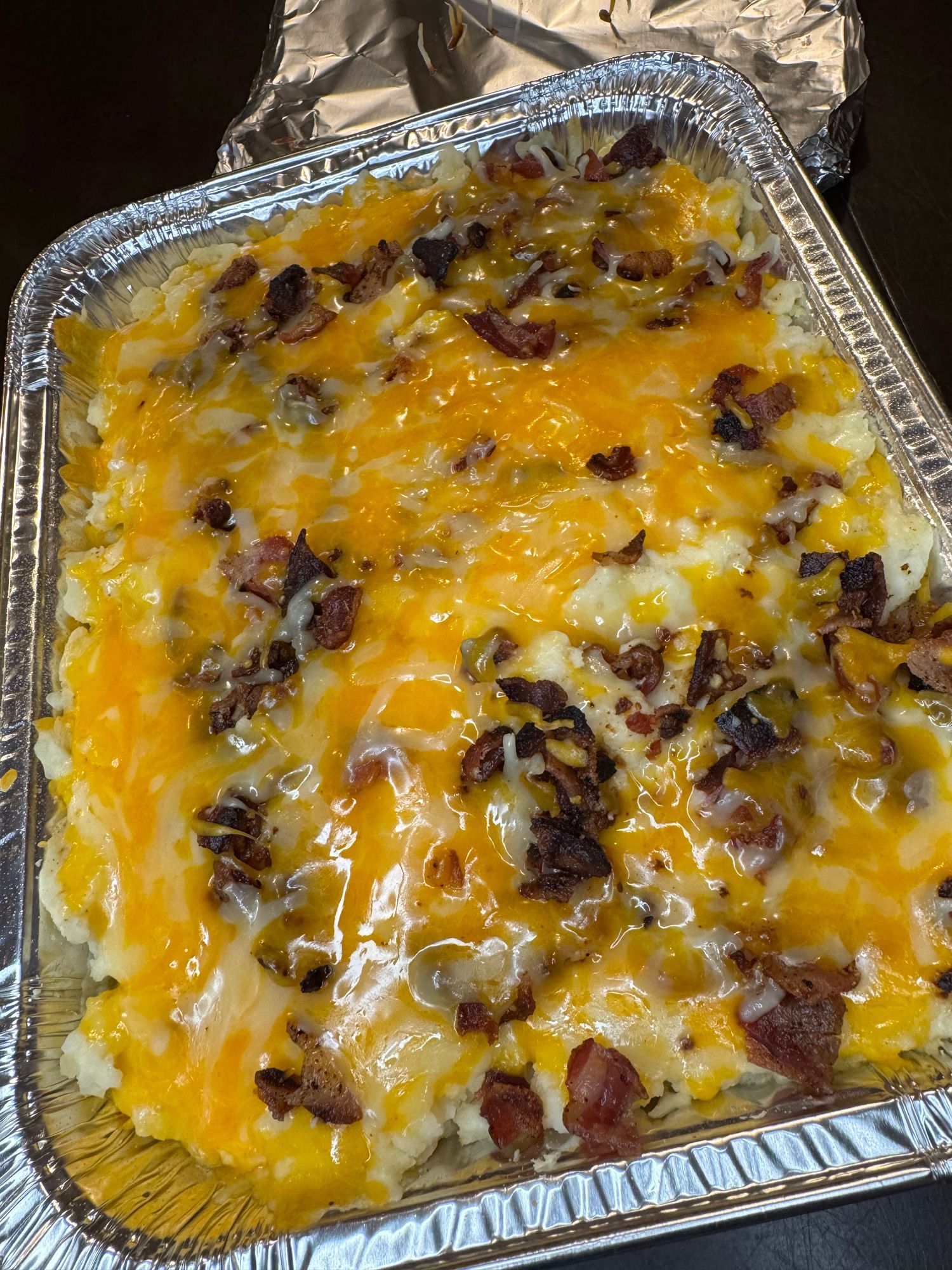 A casserole dish filled with mashed potatoes , cheese and bacon.