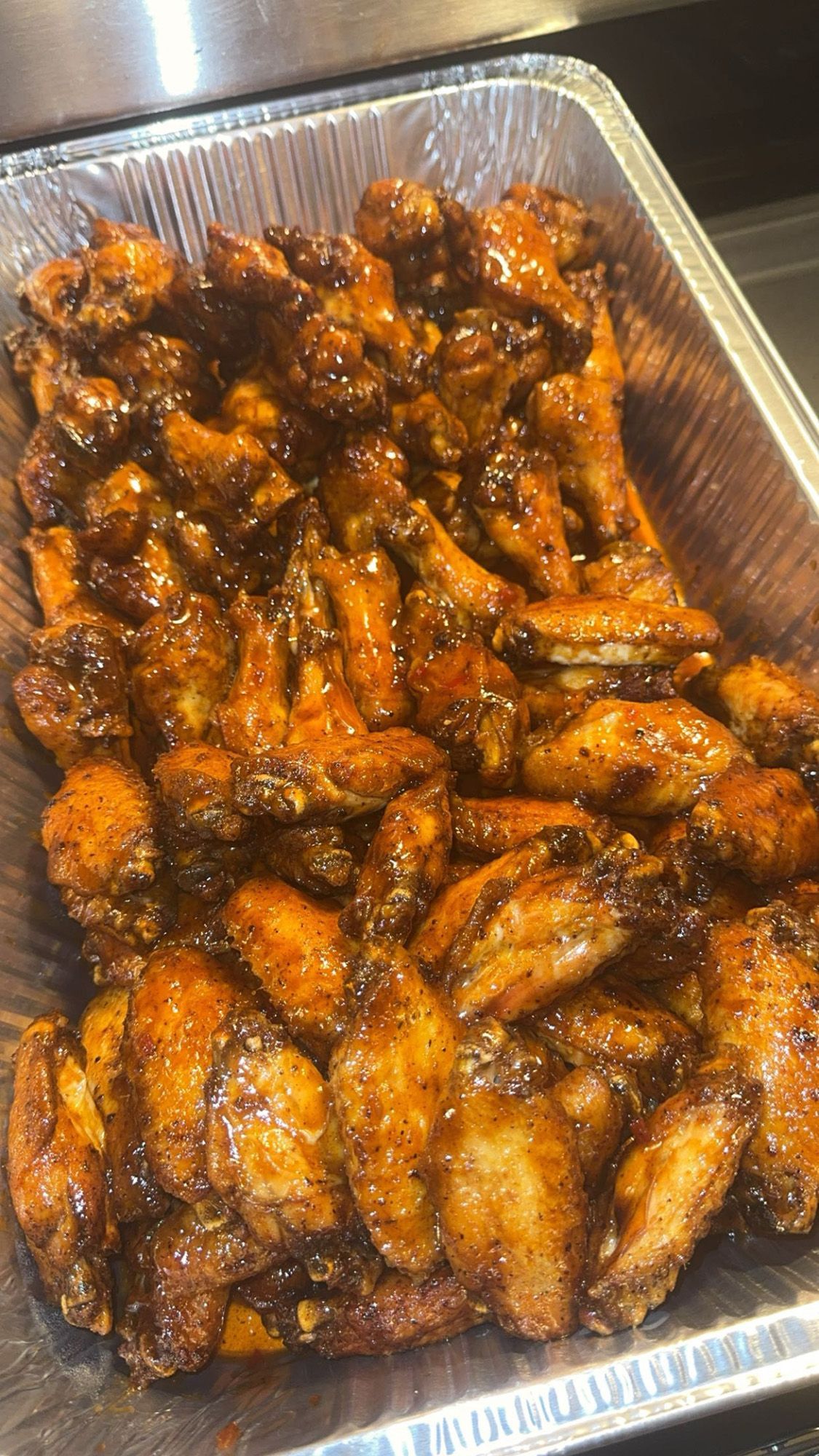A tray of chicken wings in a sauce on a table.