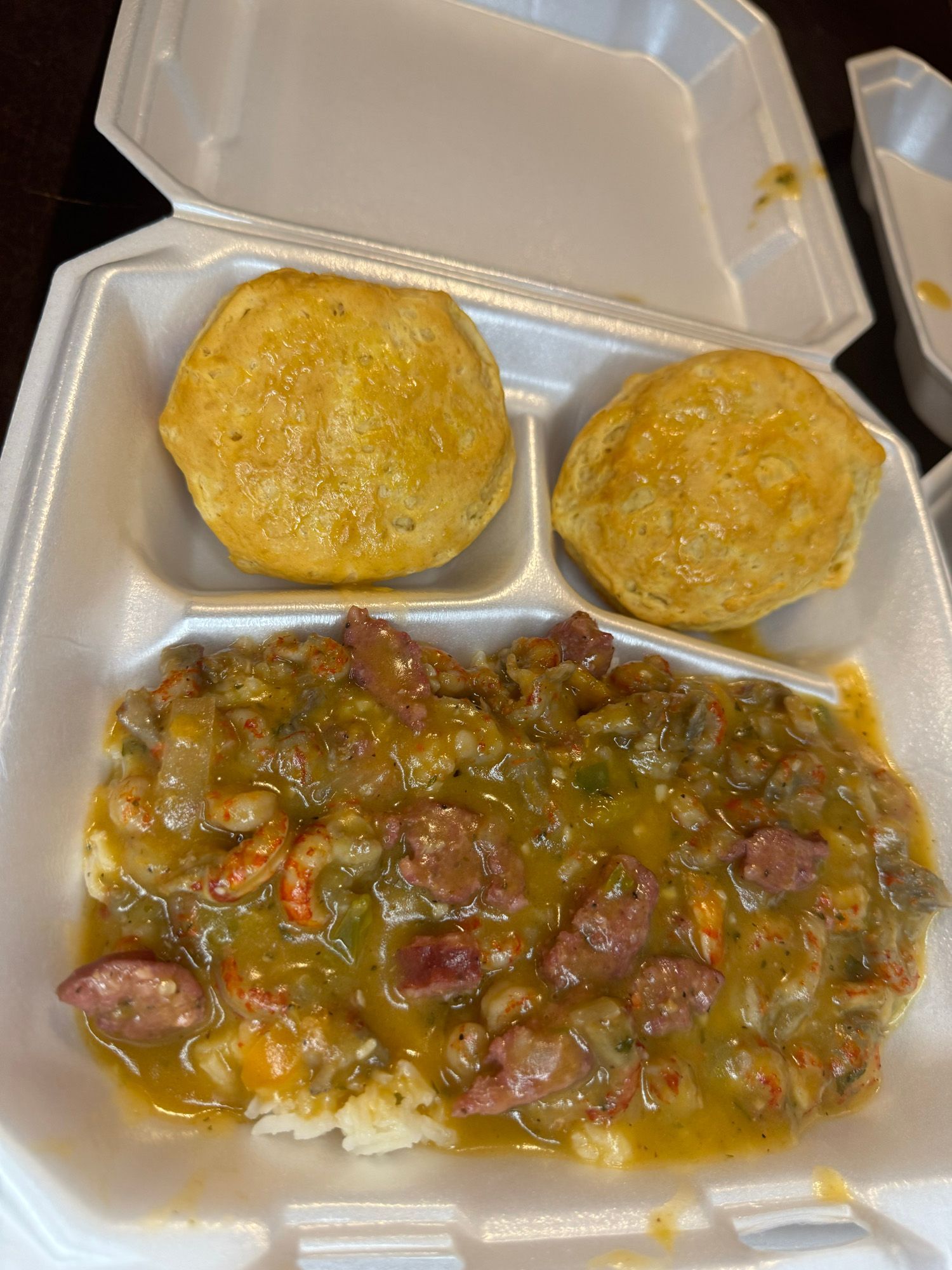 A styrofoam container filled with food and two biscuits.