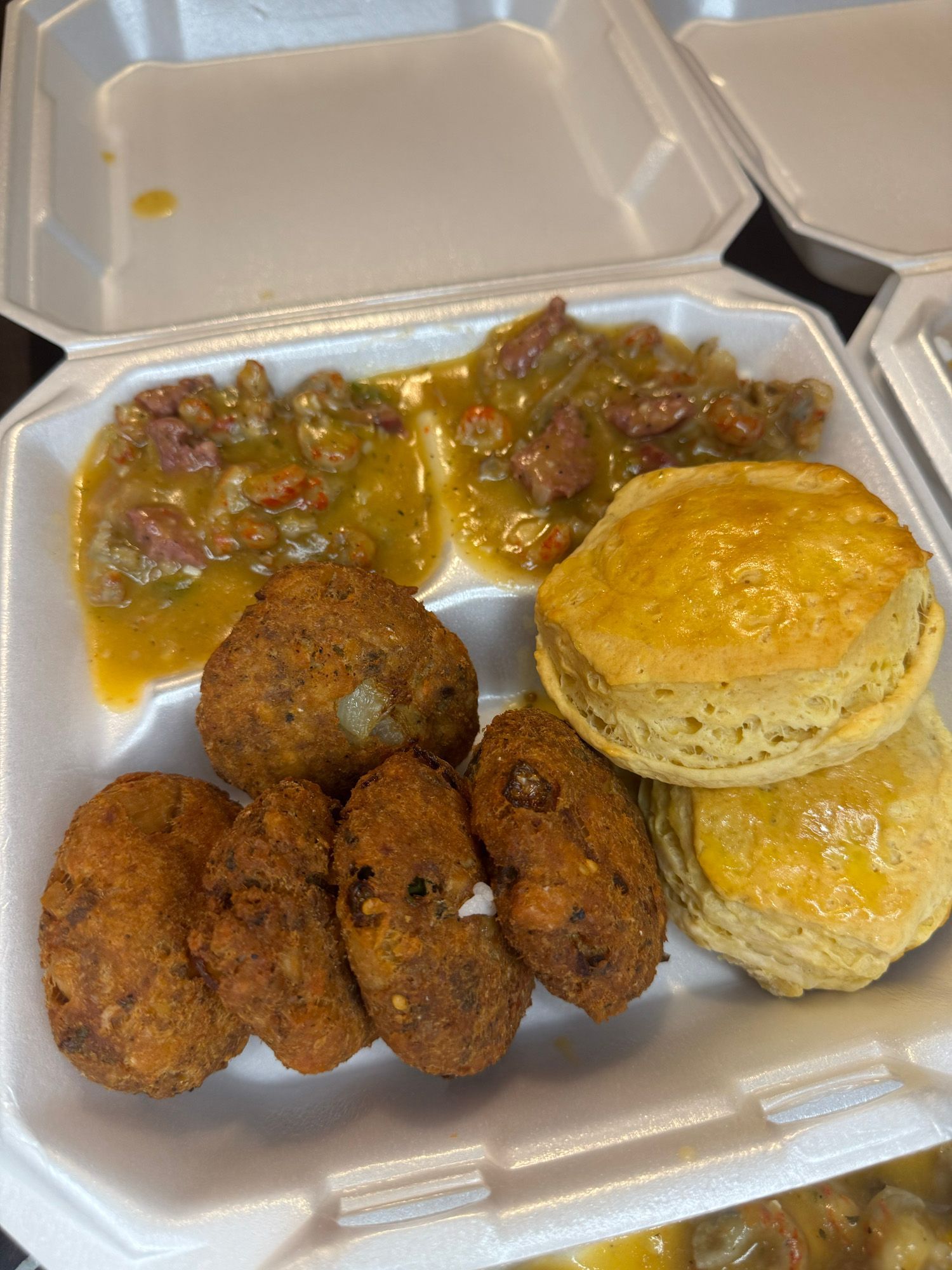 A styrofoam container filled with fried food and biscuits.