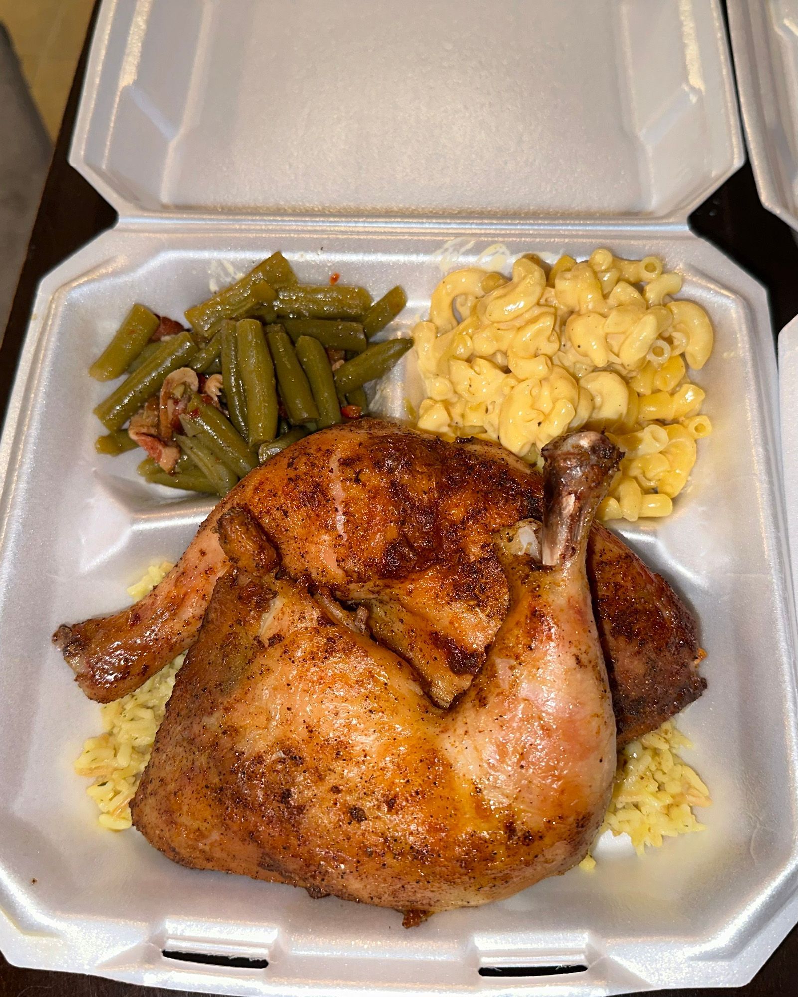A styrofoam container filled with chicken , macaroni and cheese , green beans and rice.